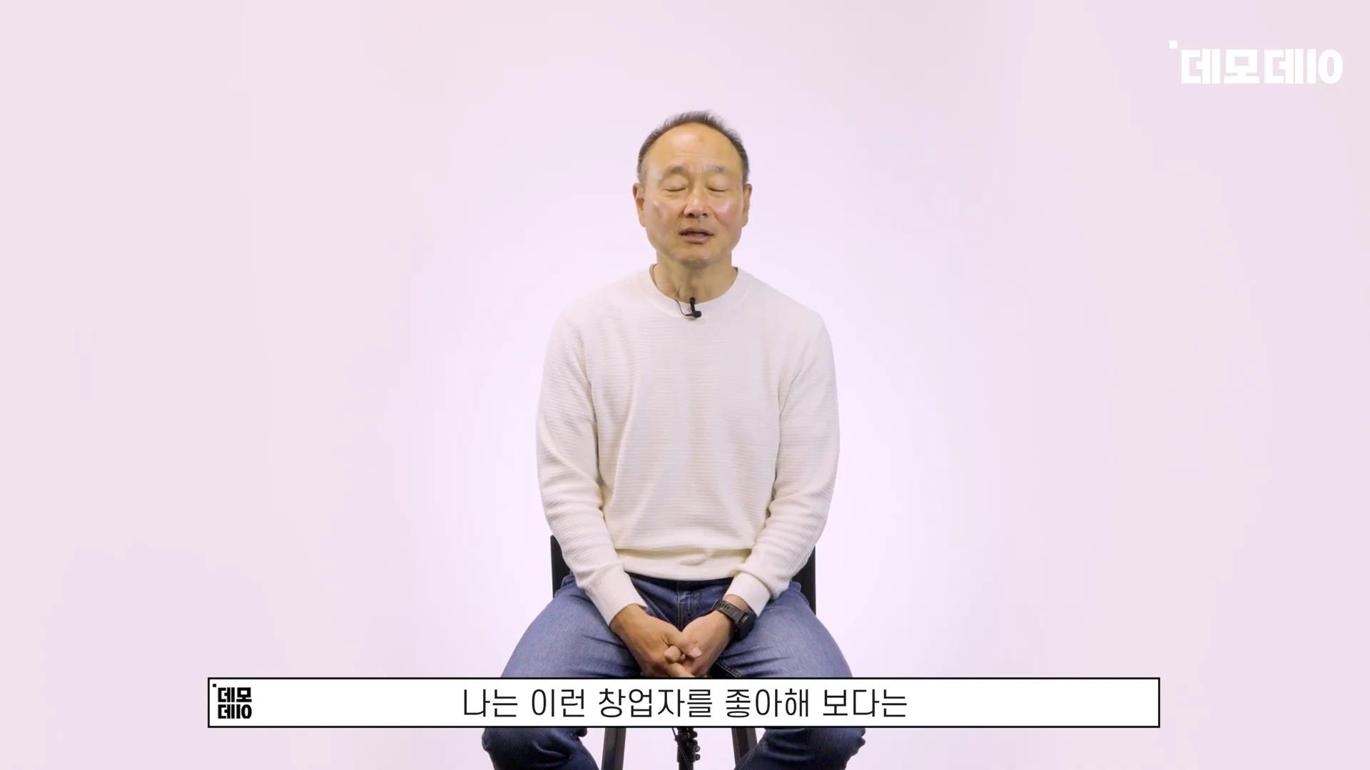 흰색 배경의 스튜디오에서 의자에 앉아 눈을 감고 이야기하는 중년 남성
