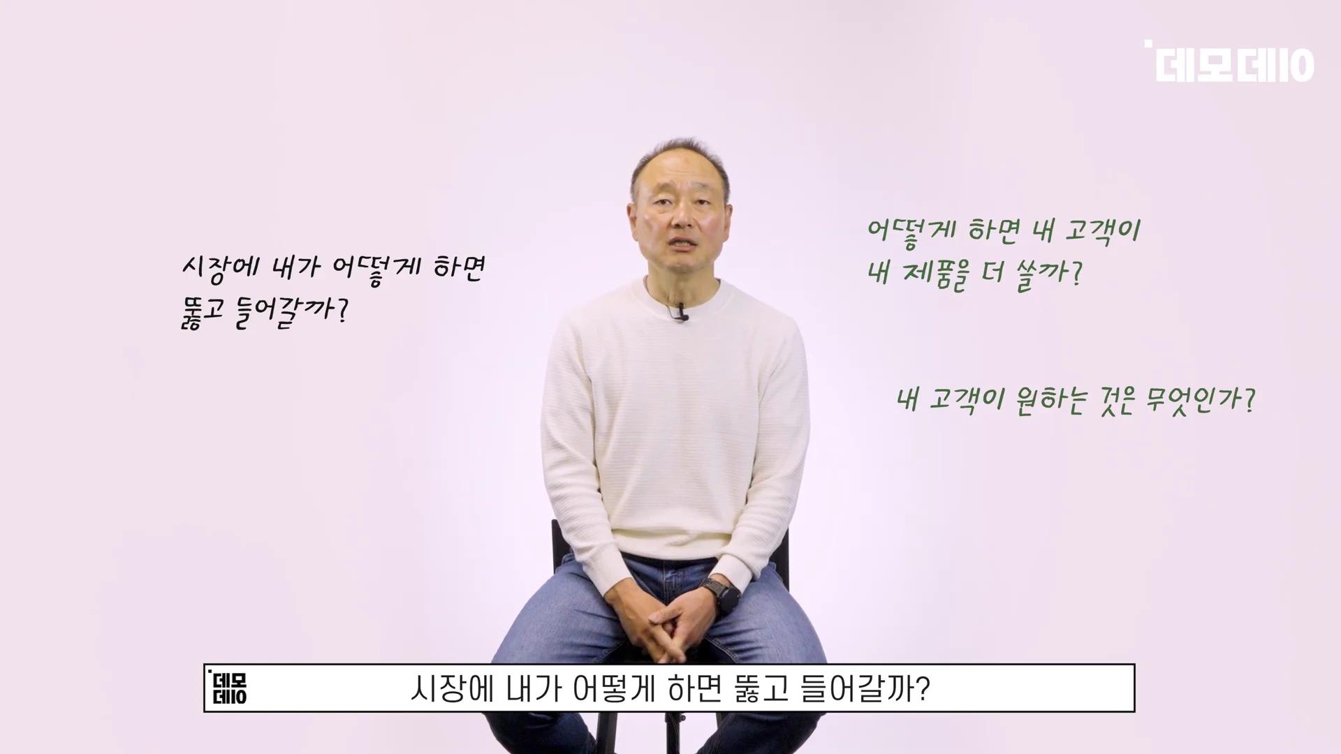흰색 니트를 입은 남성이 의자에 앉아 인터뷰를 하고 있으며, 주변에 사업의 본질에 관한 질문 문구들이 떠 있습니다.