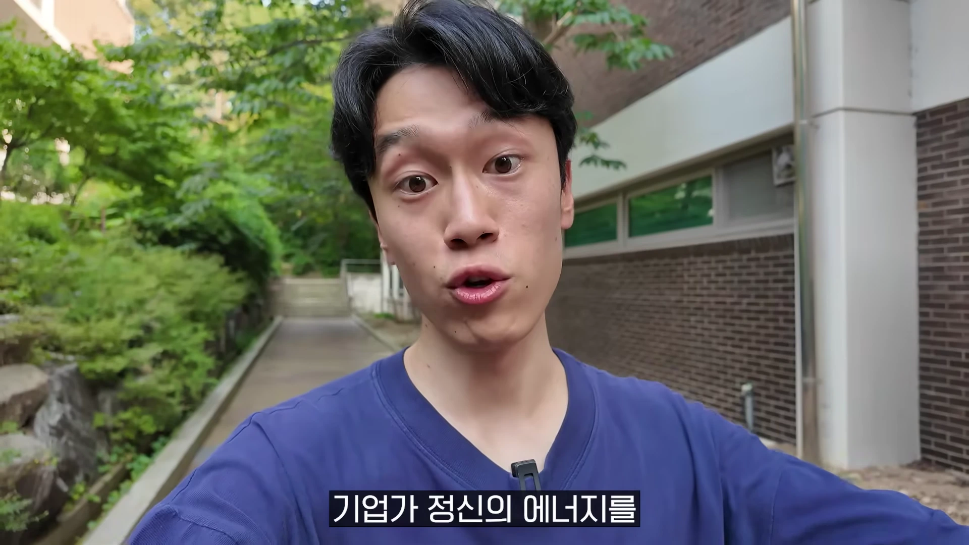 야외에서 파란색 티셔츠를 입은 남성이 카메라를 보며 이야기하고 있는 모습