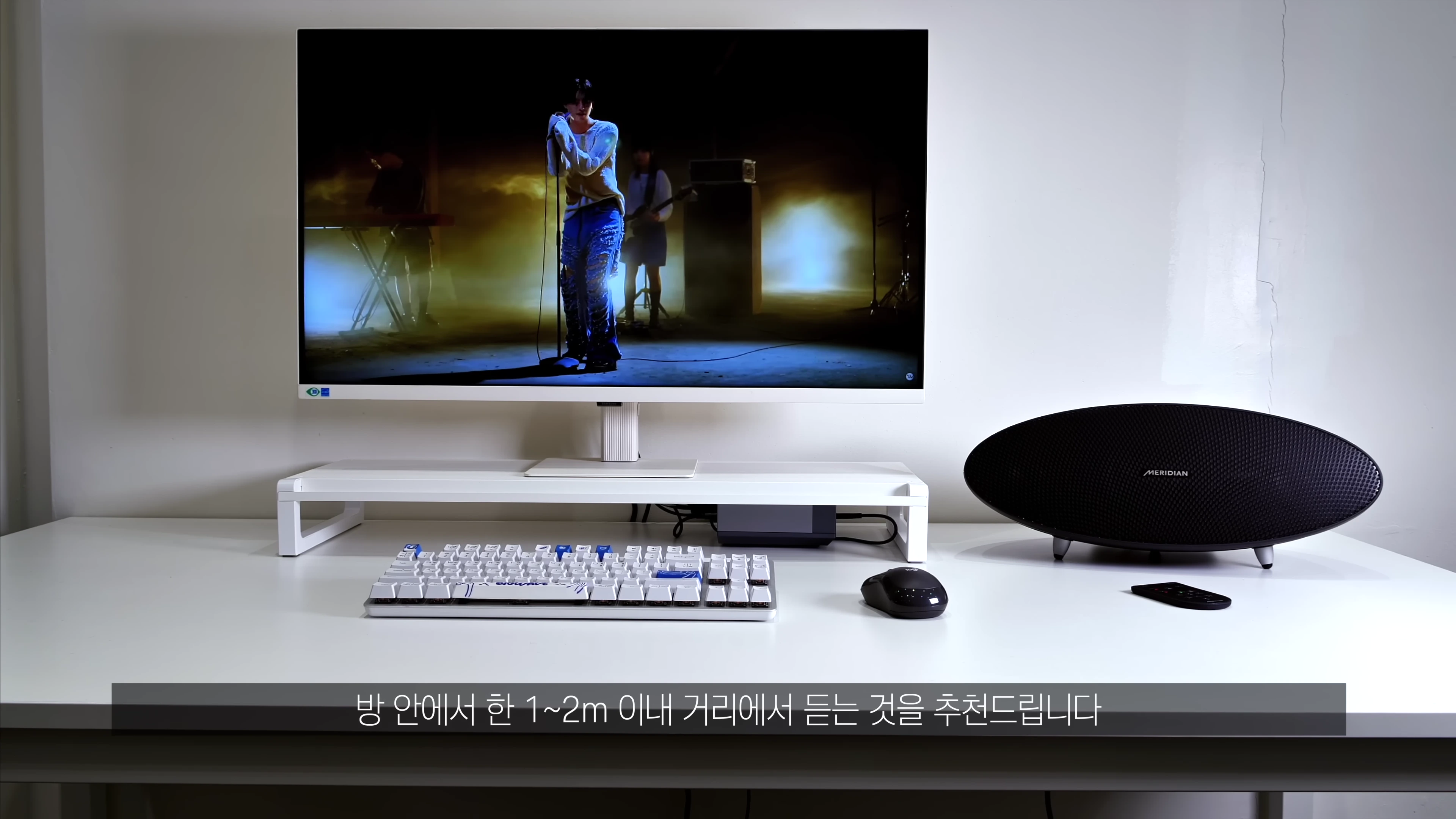 책상 위에 놓인 모니터와 타원형 스피커, 키보드, 마우스가 배치된 데스크테리어 환경
