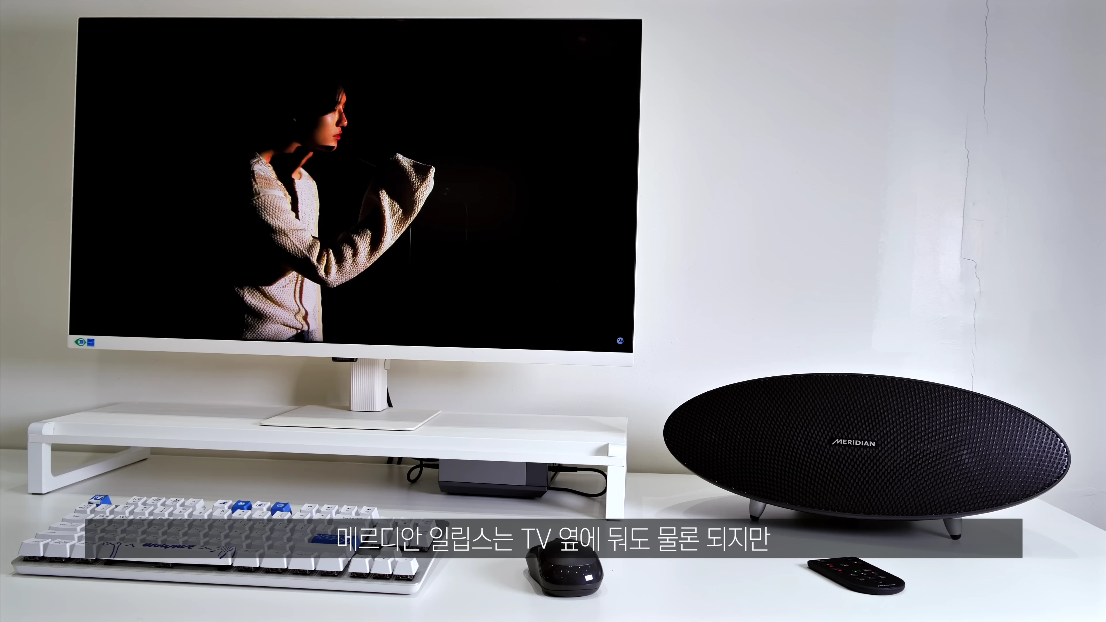 책상 위에 놓인 타원형의 검은색 메리디안 일립스 스피커와 그 옆의 모니터 및 키보드
