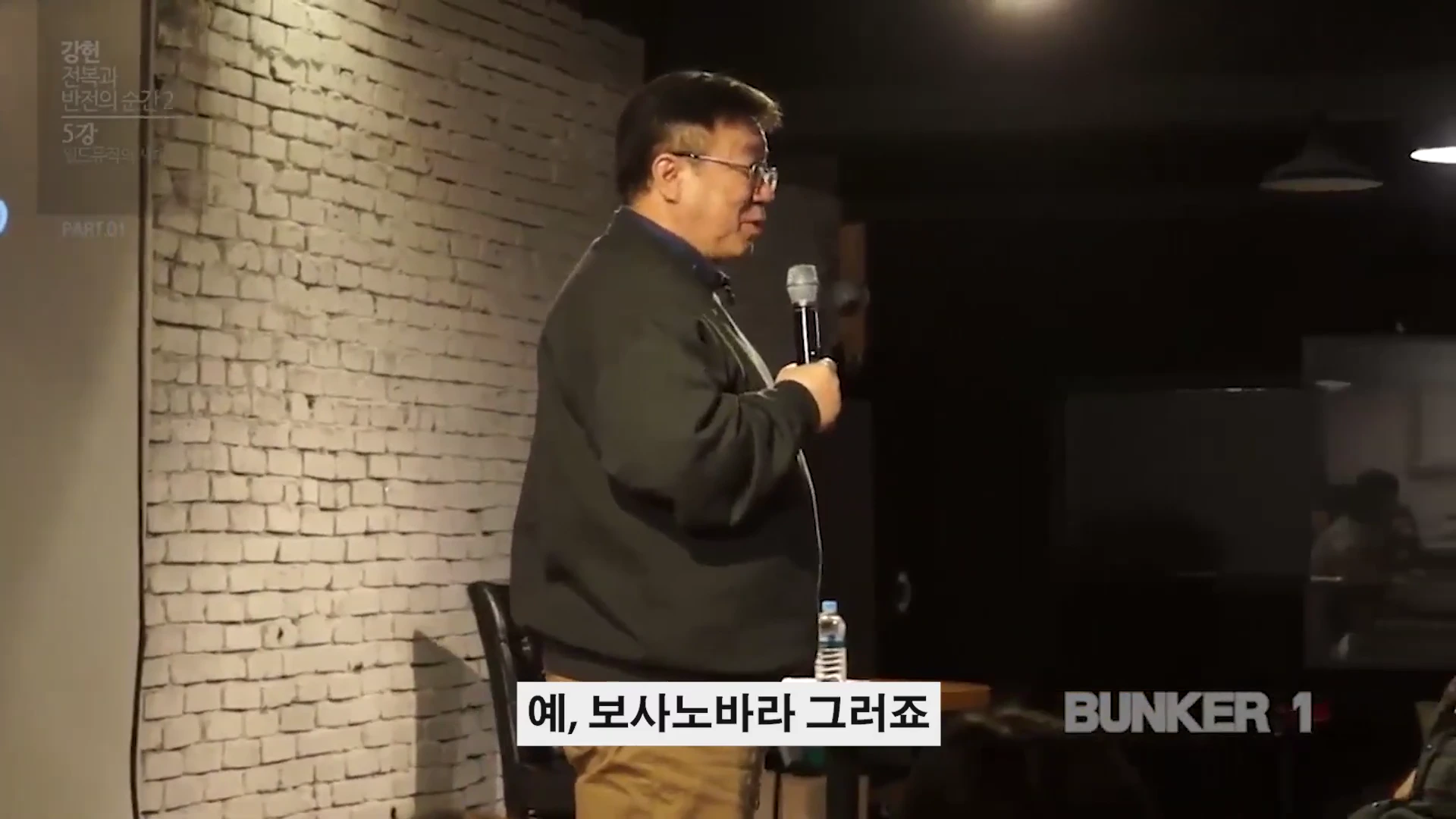 강연장에서 마이크를 잡고 서 있는 중년 남성 강연자