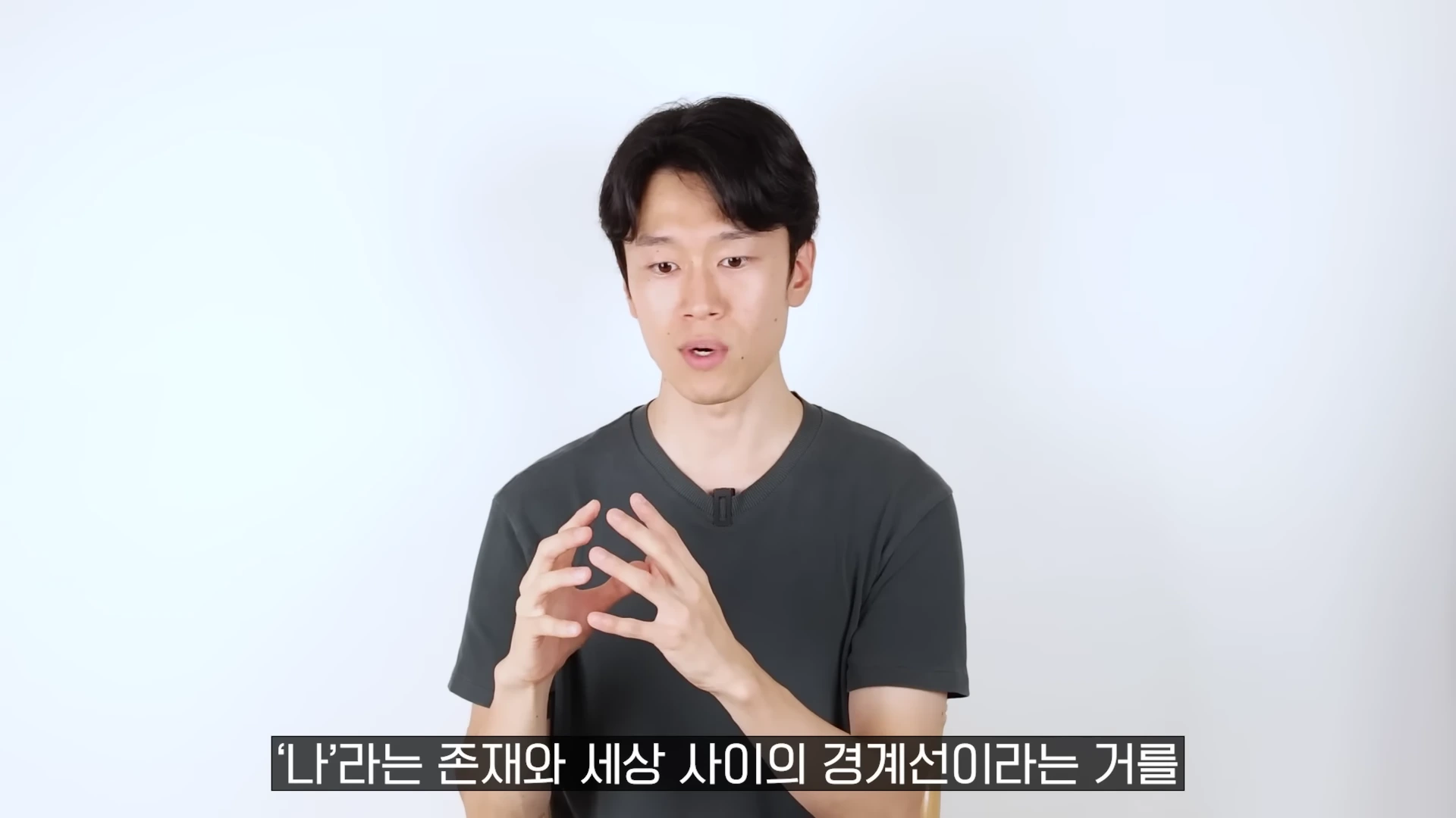 흰 배경 앞에서 검은색 티셔츠를 입은 남성이 손을 모으고 진지하게 이야기하고 있다.