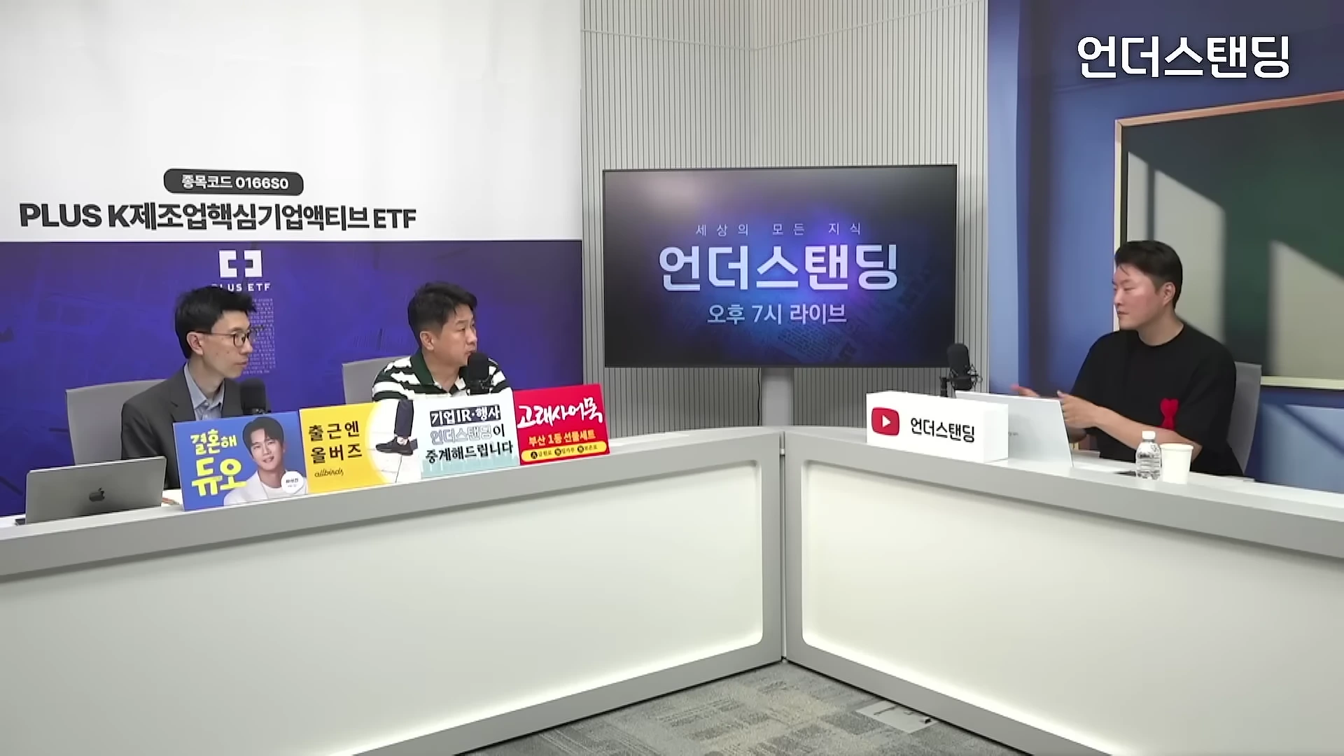 스튜디오에 앉아 대화를 나누는 세 명의 남성과 대형 모니터가 있는 방송 세트장