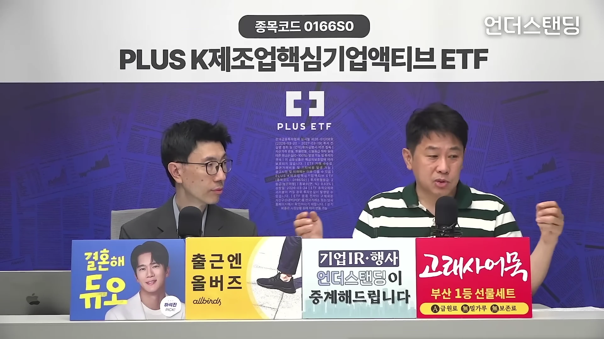 스튜디오에서 두 명의 남성이 마이크를 앞에 두고 대화를 나누고 있으며, 앞쪽에는 다양한 광고 문구가 적힌 패널들이 놓여 있다.
