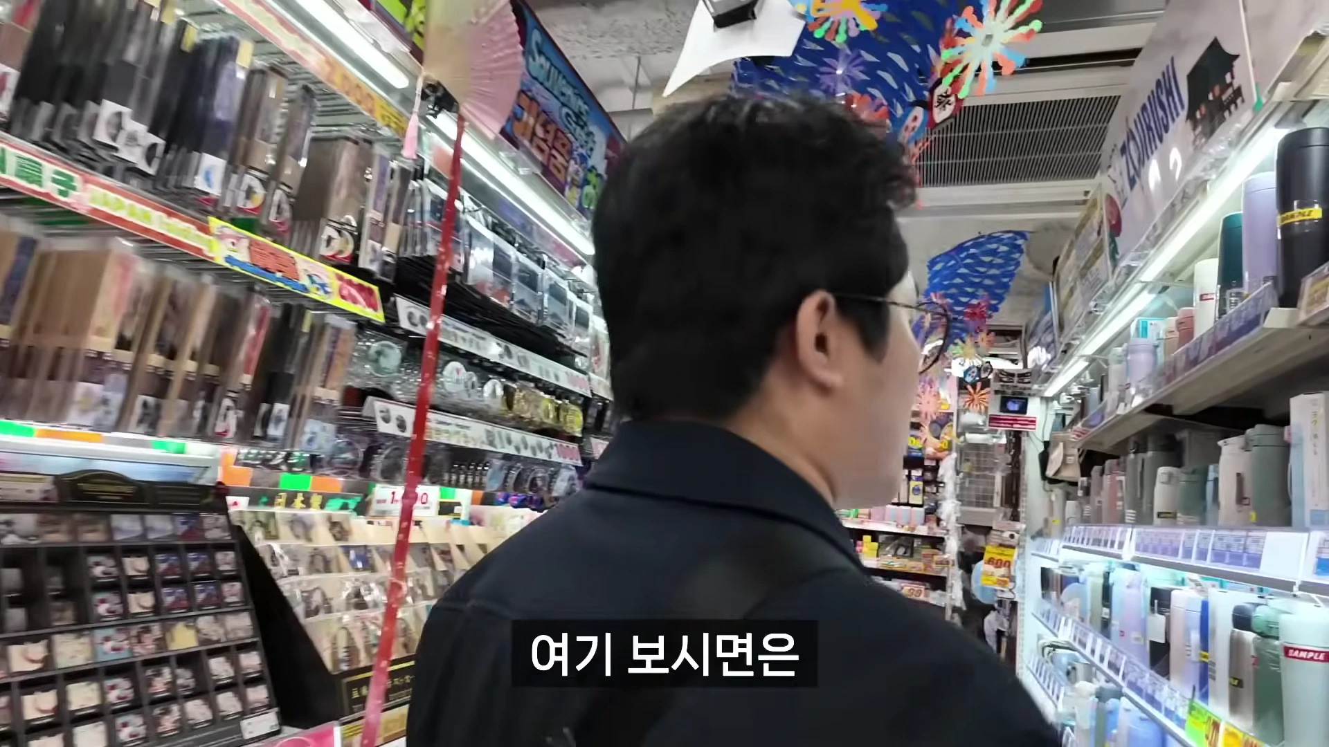 안경을 쓴 남성이 다양한 상품이 빼곡하게 진열된 매장 통로를 걸으며 둘러보고 있다.