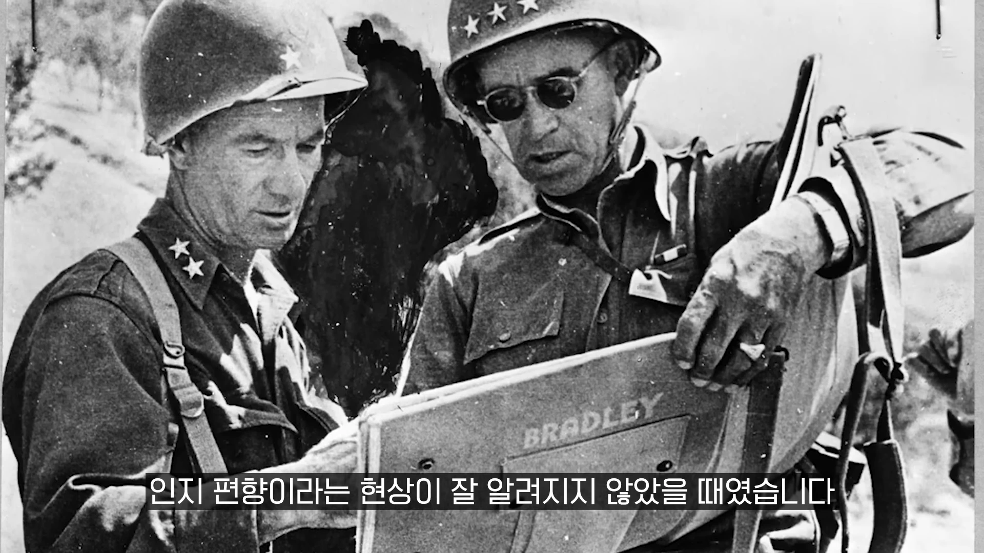 군복을 입고 철모를 쓴 두 장교가 야외에서 지도를 보며 논의하는 흑백 사진