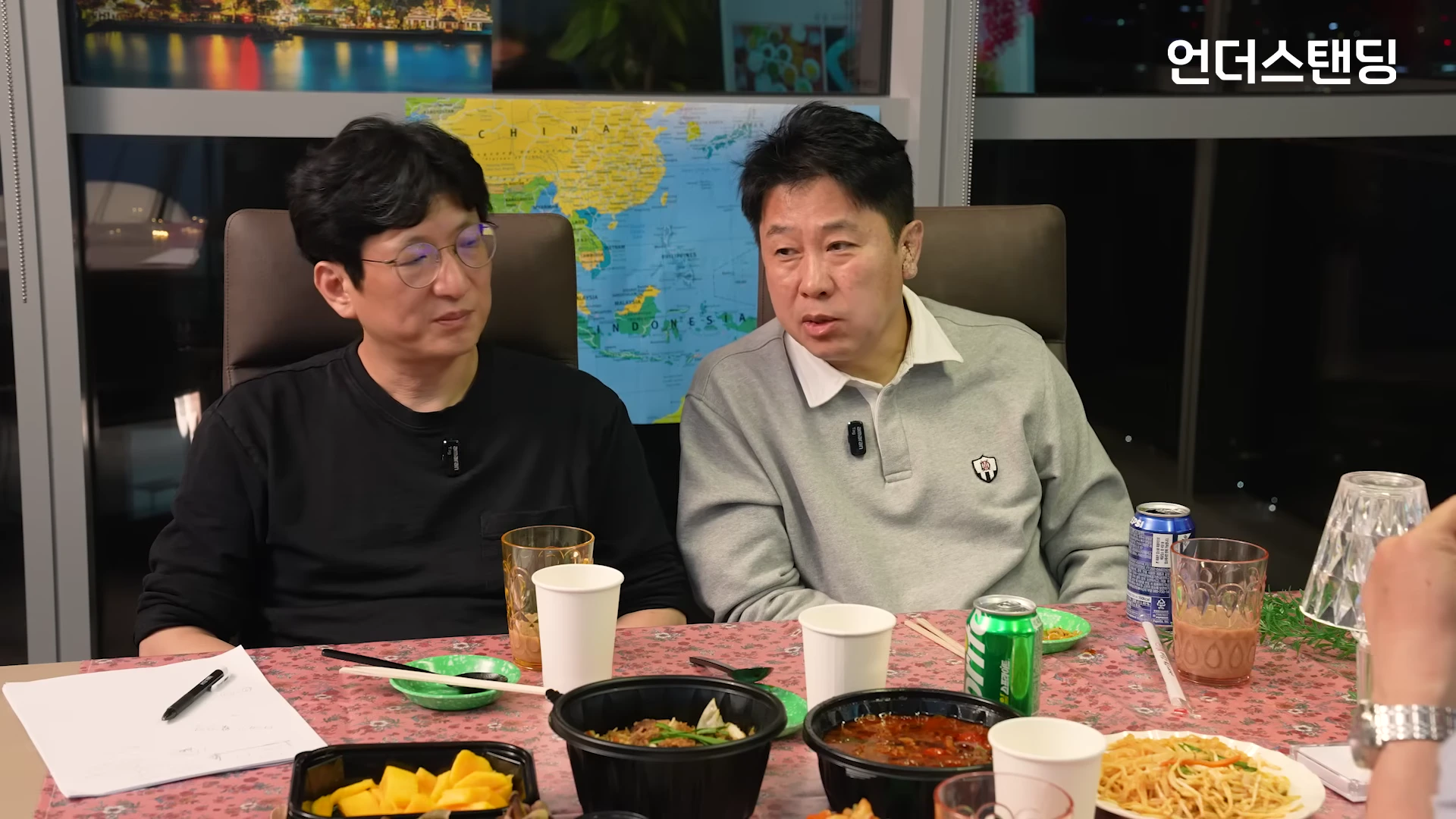 스튜디오 테이블에 앉아 대화를 나누는 두 남성과 그 앞에 놓인 다양한 동남아 음식들