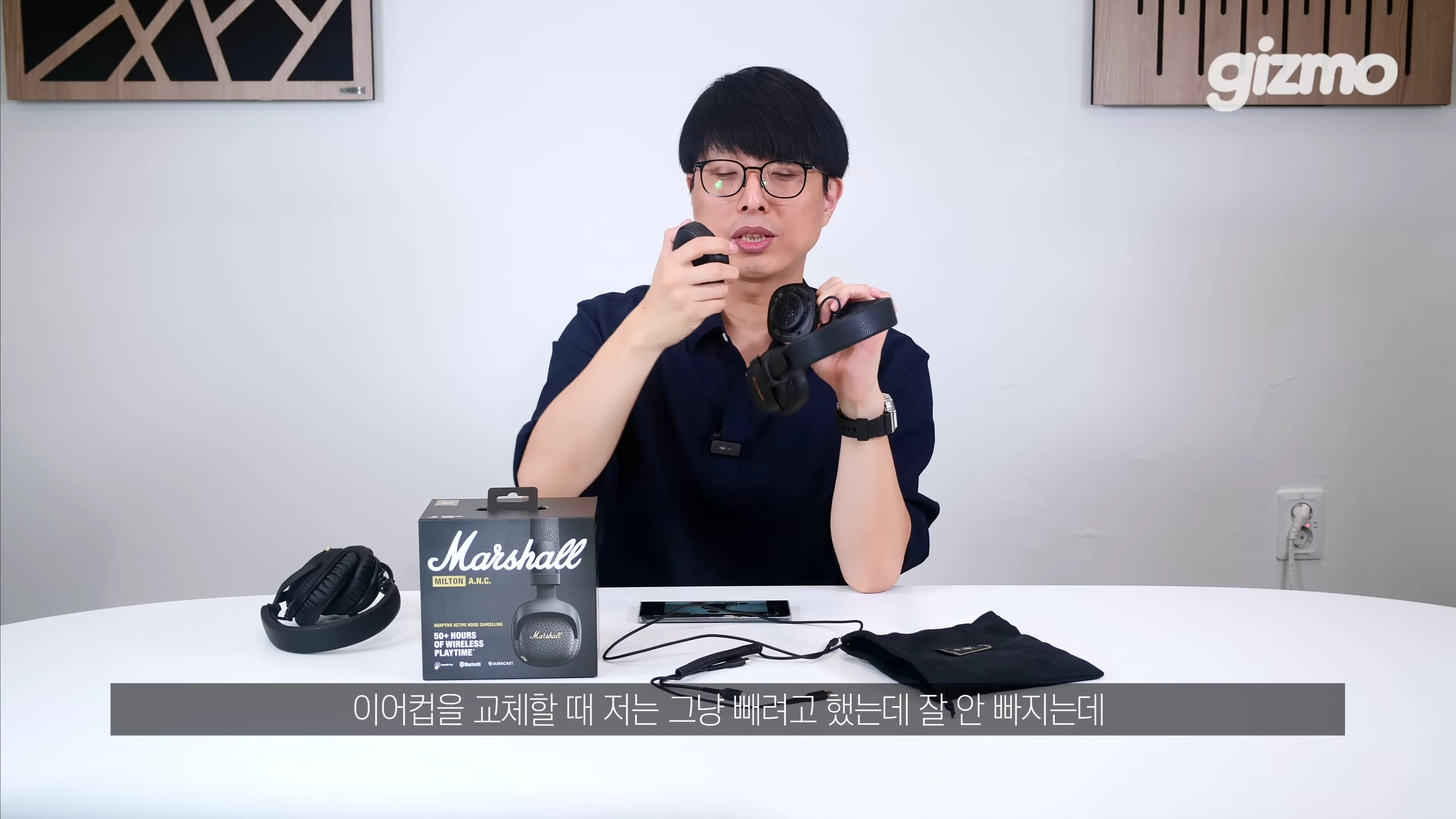 안경을 쓴 남성이 테이블 위에서 마샬 헤드폰의 이어패드를 분리하는 방법을 보여주고 있다.
