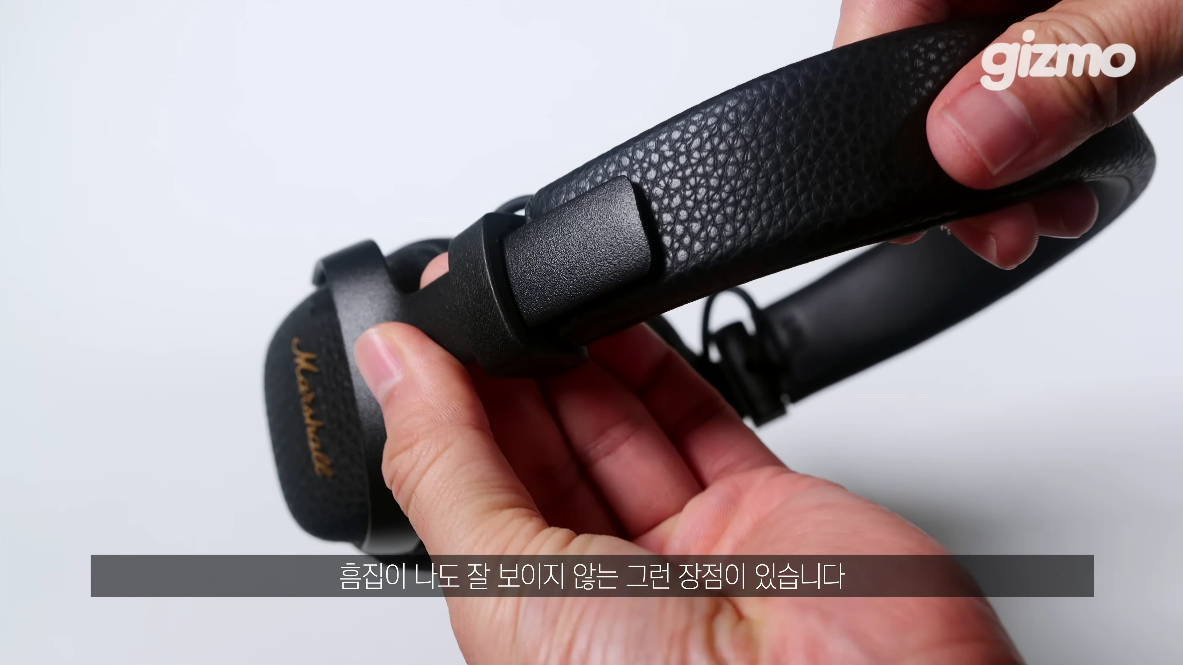 손으로 마샬 헤드폰의 가죽 질감 헤드밴드와 이음부를 만지며 보여주는 모습