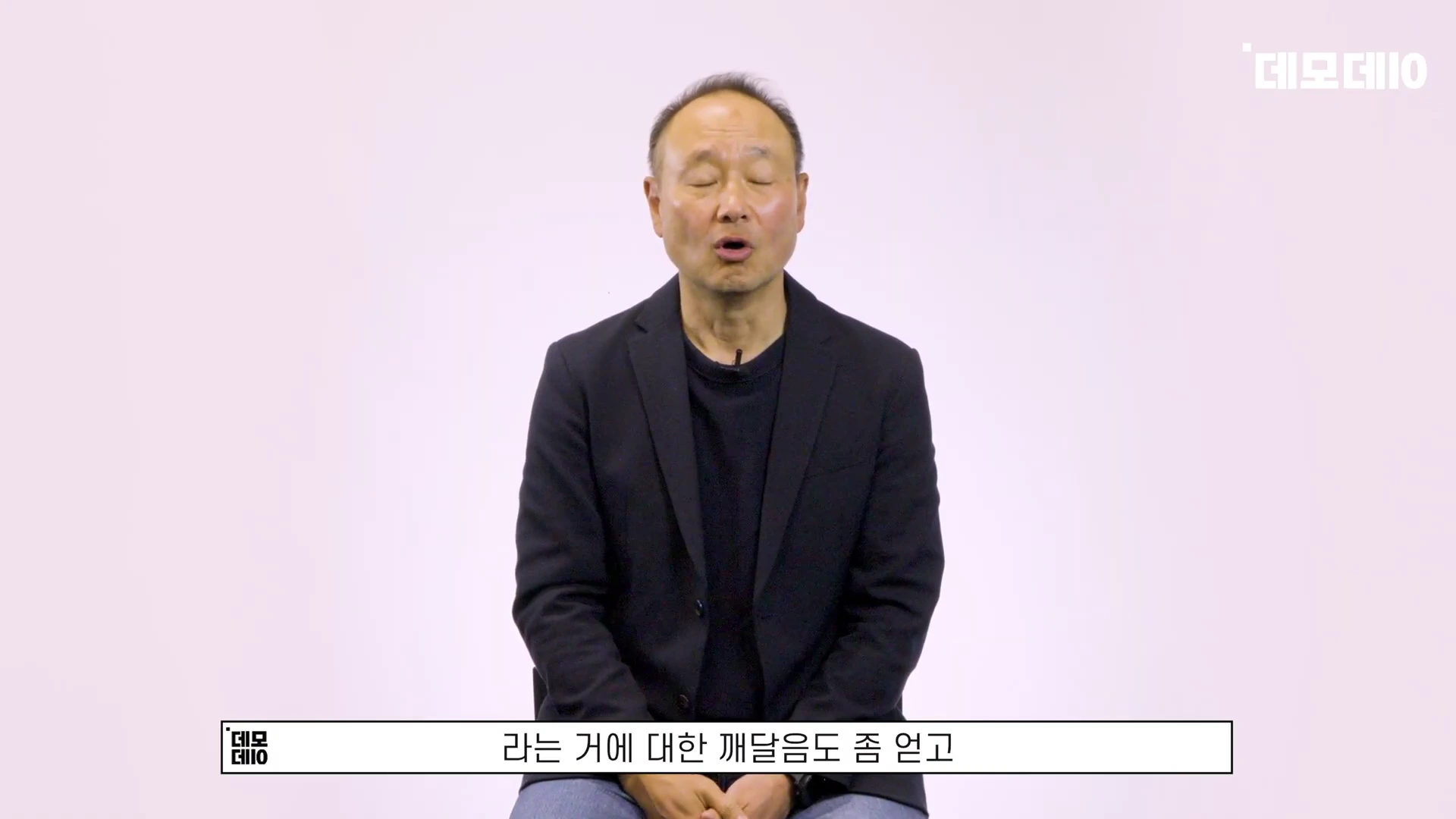 흰 배경 앞에 앉아 진지하게 이야기하는 중년 남성