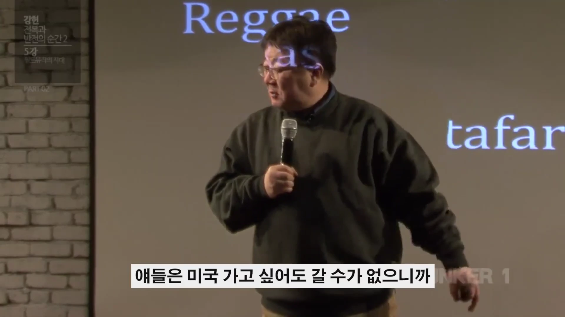 강연자가 마이크를 들고 서 있으며 뒤편 스크린에는 레게와 관련된 단어들이 투사되어 있다.