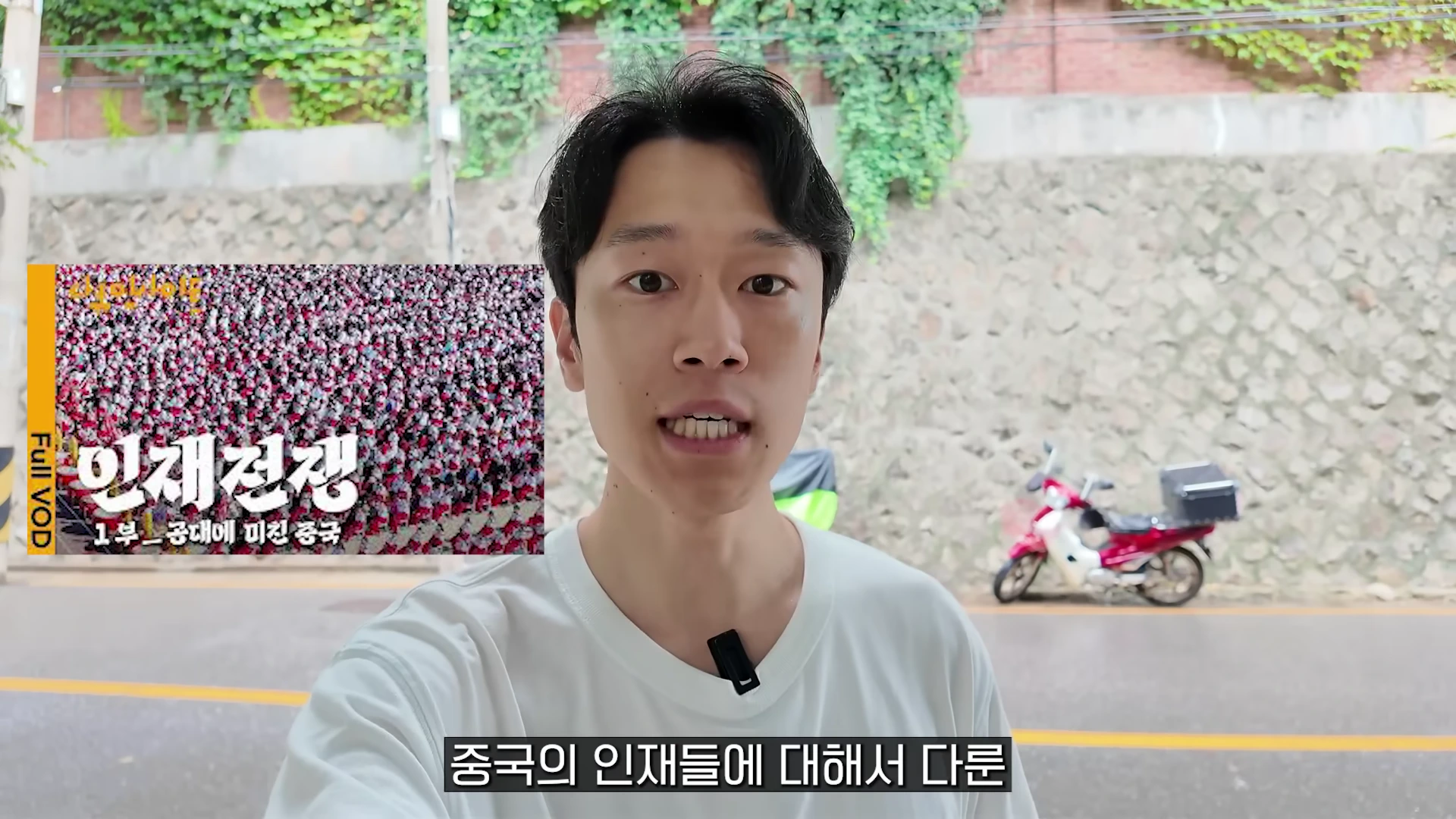 야외에서 흰색 티셔츠를 입은 남성이 카메라를 보며 이야기하고 있고, 화면 왼쪽에는 '인재전쟁'이라는 제목의 영상 자료 화면이 떠 있다.