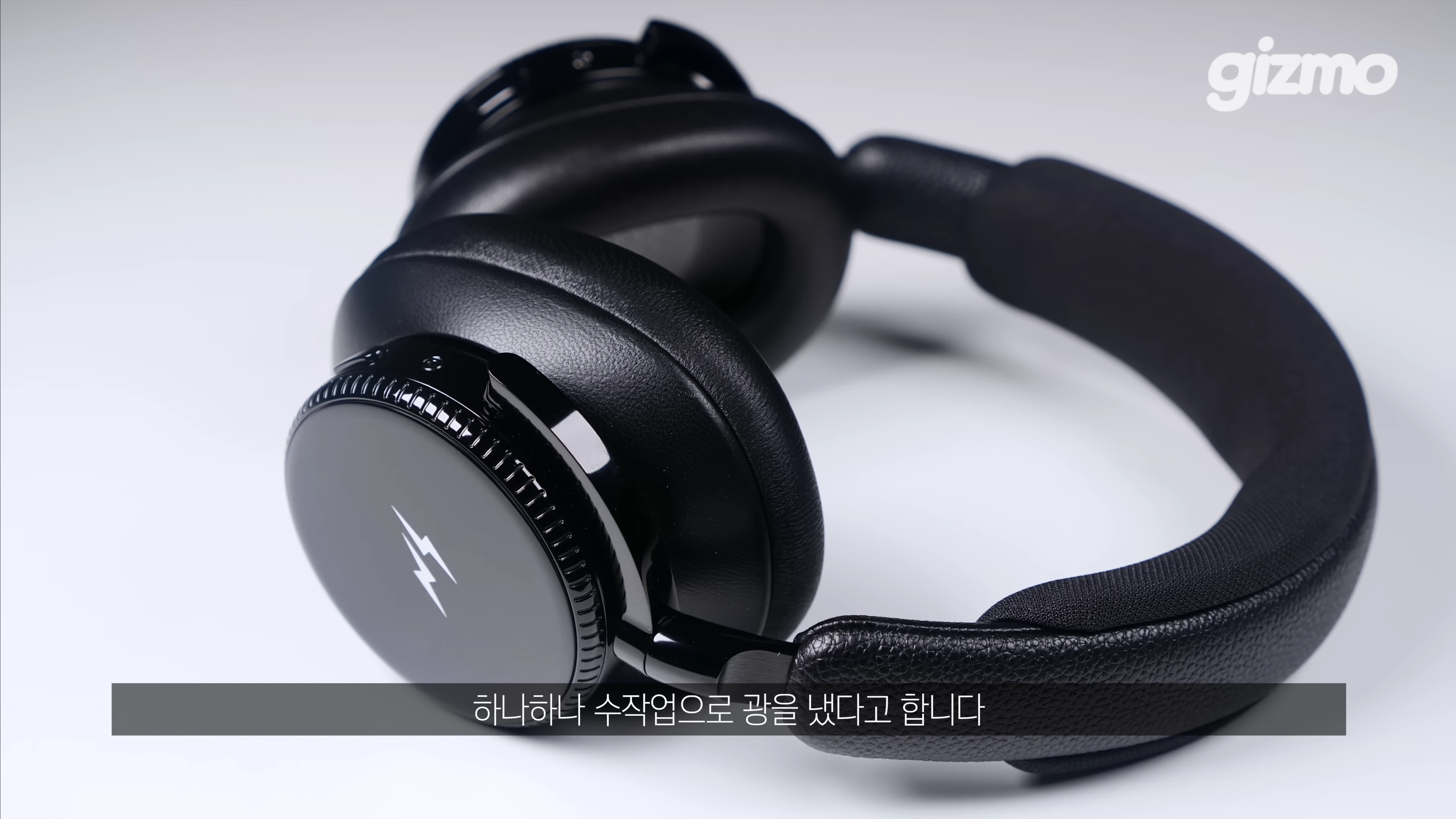 번개 로고가 새겨진 검은색 유광 헤드폰이 흰색 배경 위에 놓여 있다.