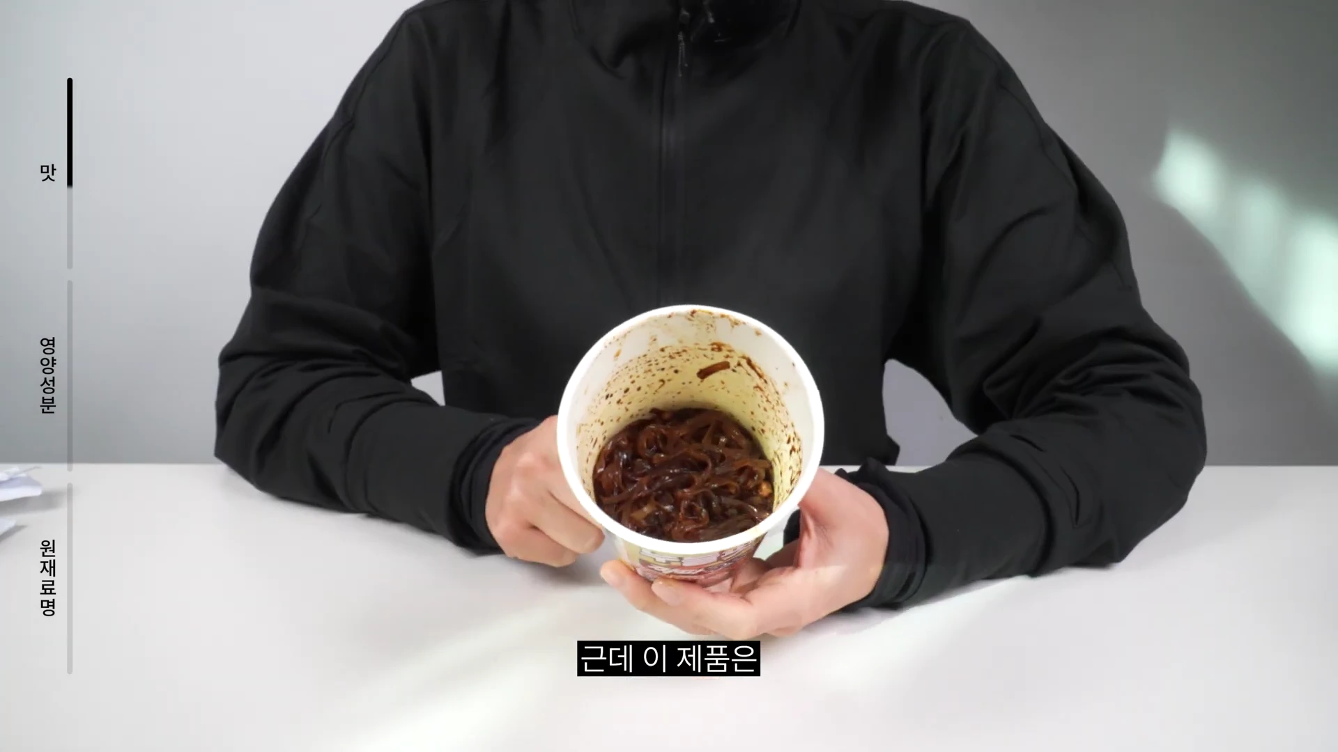 검은색 집업을 입은 사람이 짜장 소스가 묻은 컵라면 용기를 양손으로 들어 보여주고 있다.