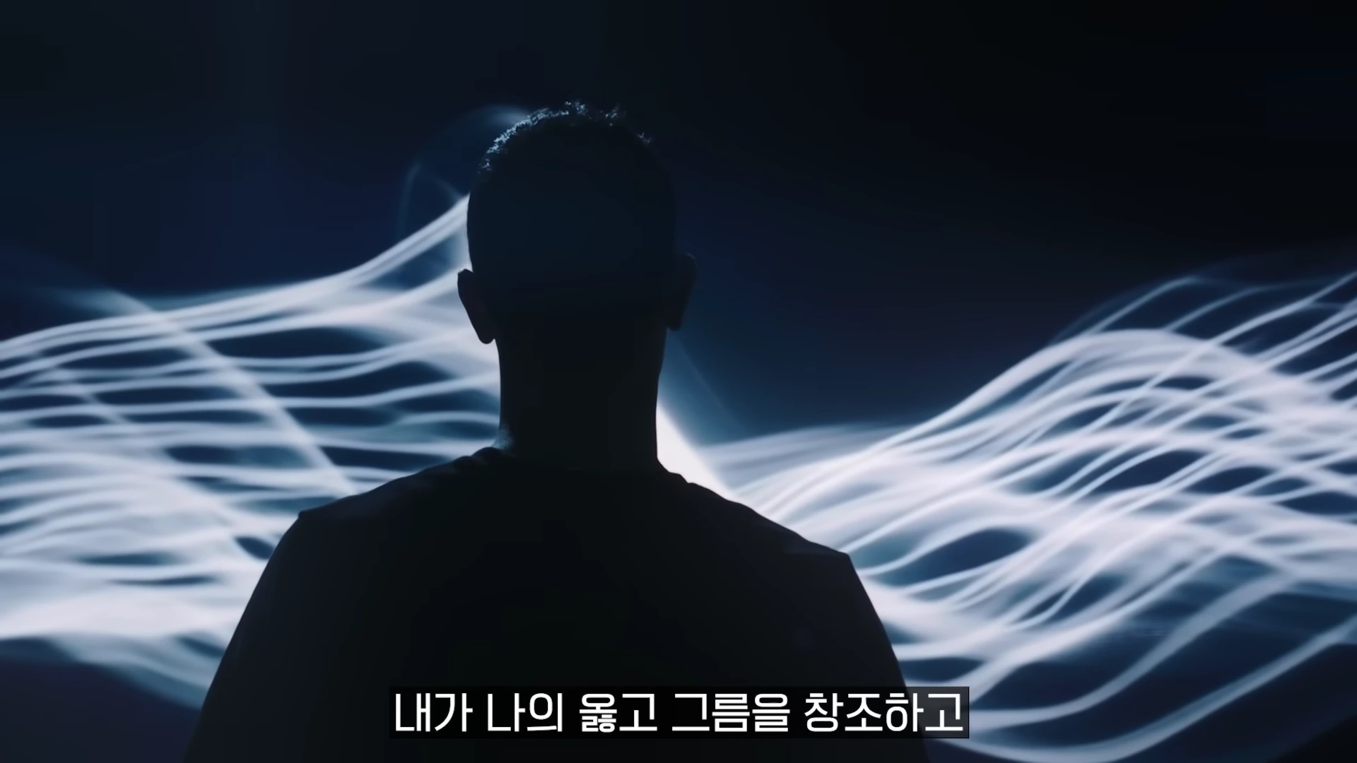 어두운 배경 속에서 실루엣으로만 보이는 사람 뒤로 빛나는 물결 모양의 선들이 흐르고 있다.