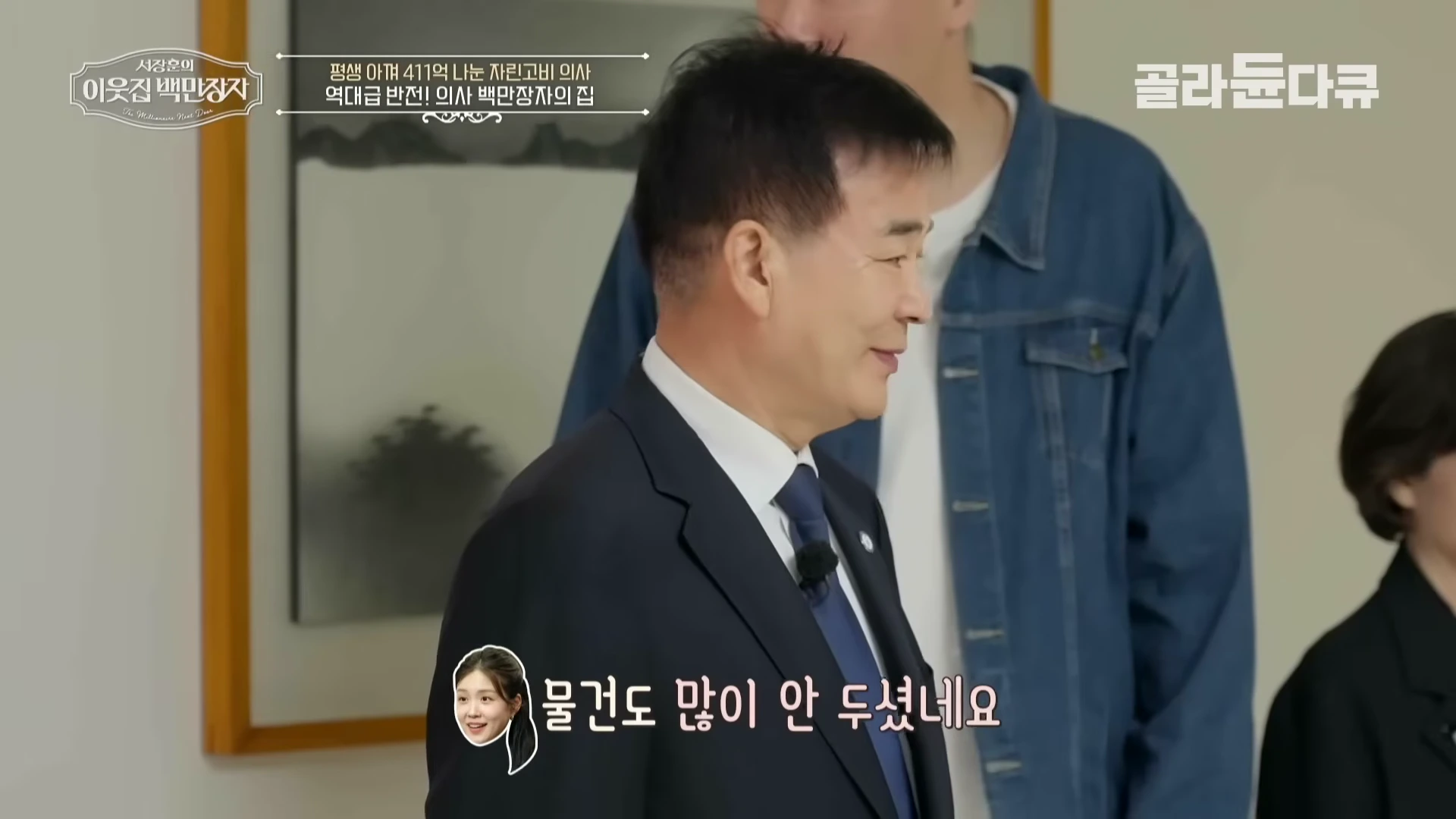 정장을 입은 중년 남성이 실내에서 미소 짓고 있으며, 화면 상단에는 프로그램 로고와 자막이 배치되어 있다.
