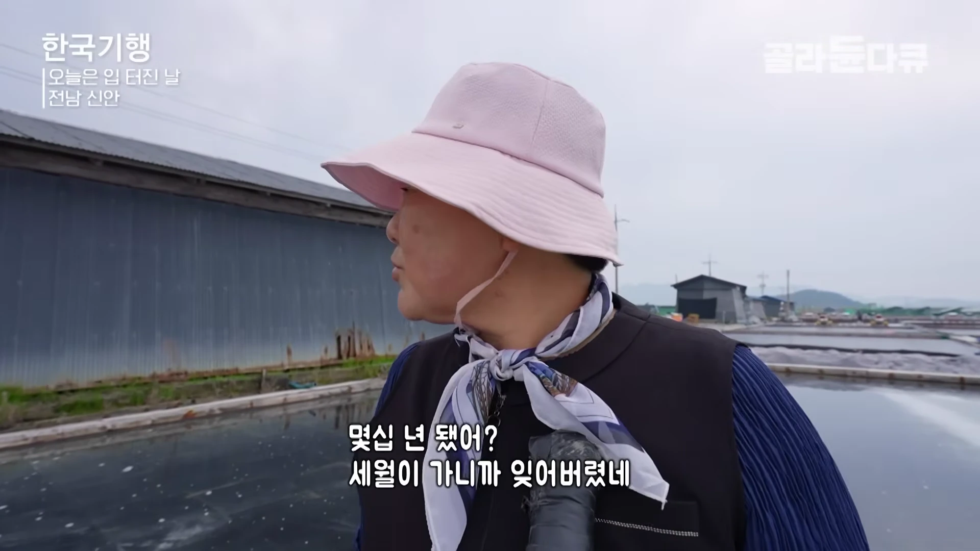 분홍색 벙거지 모자를 쓴 중년 여성이 염전 배경으로 서 있는 모습