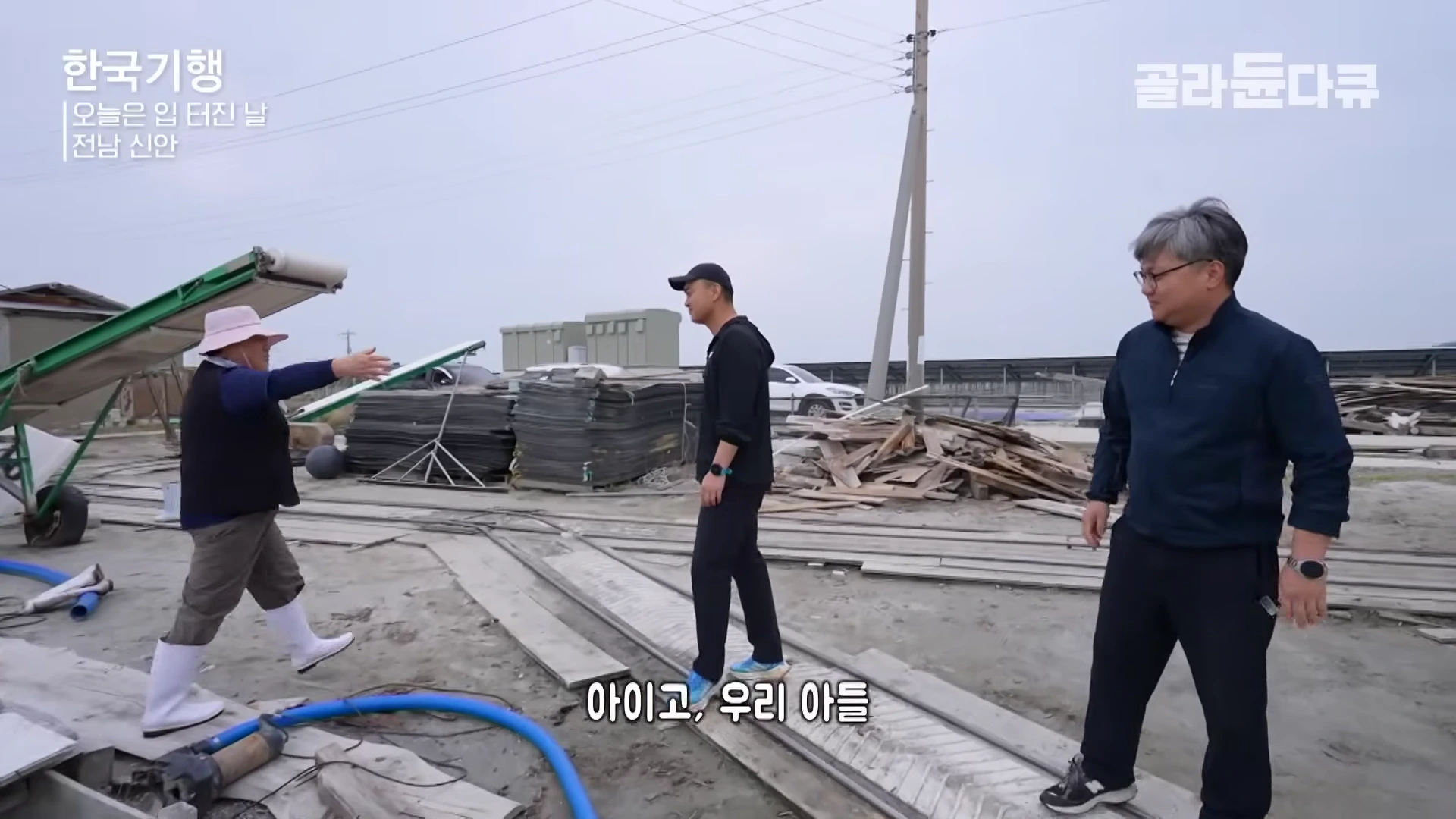 염전에서 일하는 중년 여성과 방문한 아들, 그리고 다른 남성이 야외에서 대화를 나누고 있는 모습