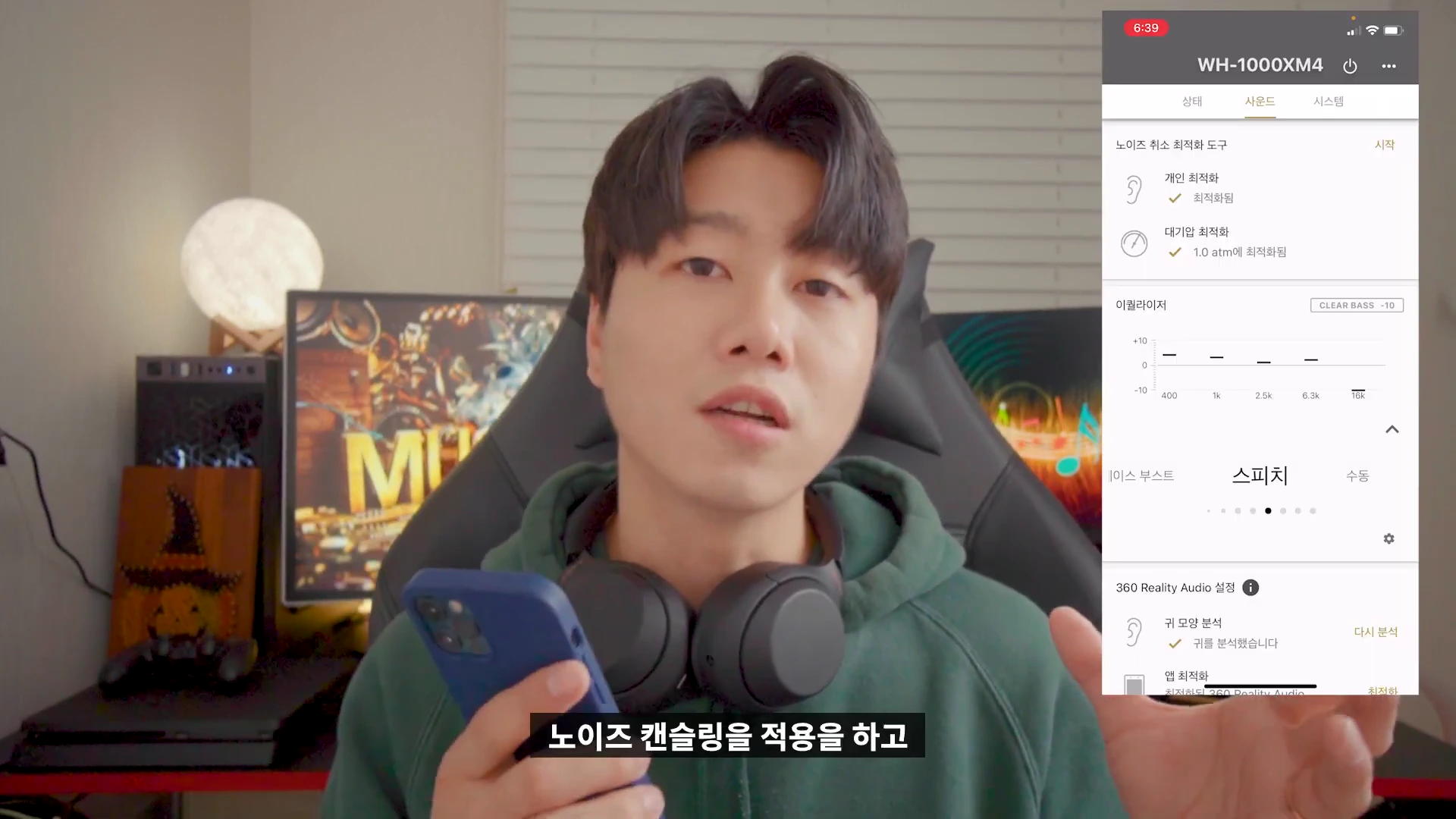 헤드폰을 목에 건 남성이 스마트폰 앱 화면을 가리키며 설명하는 모습