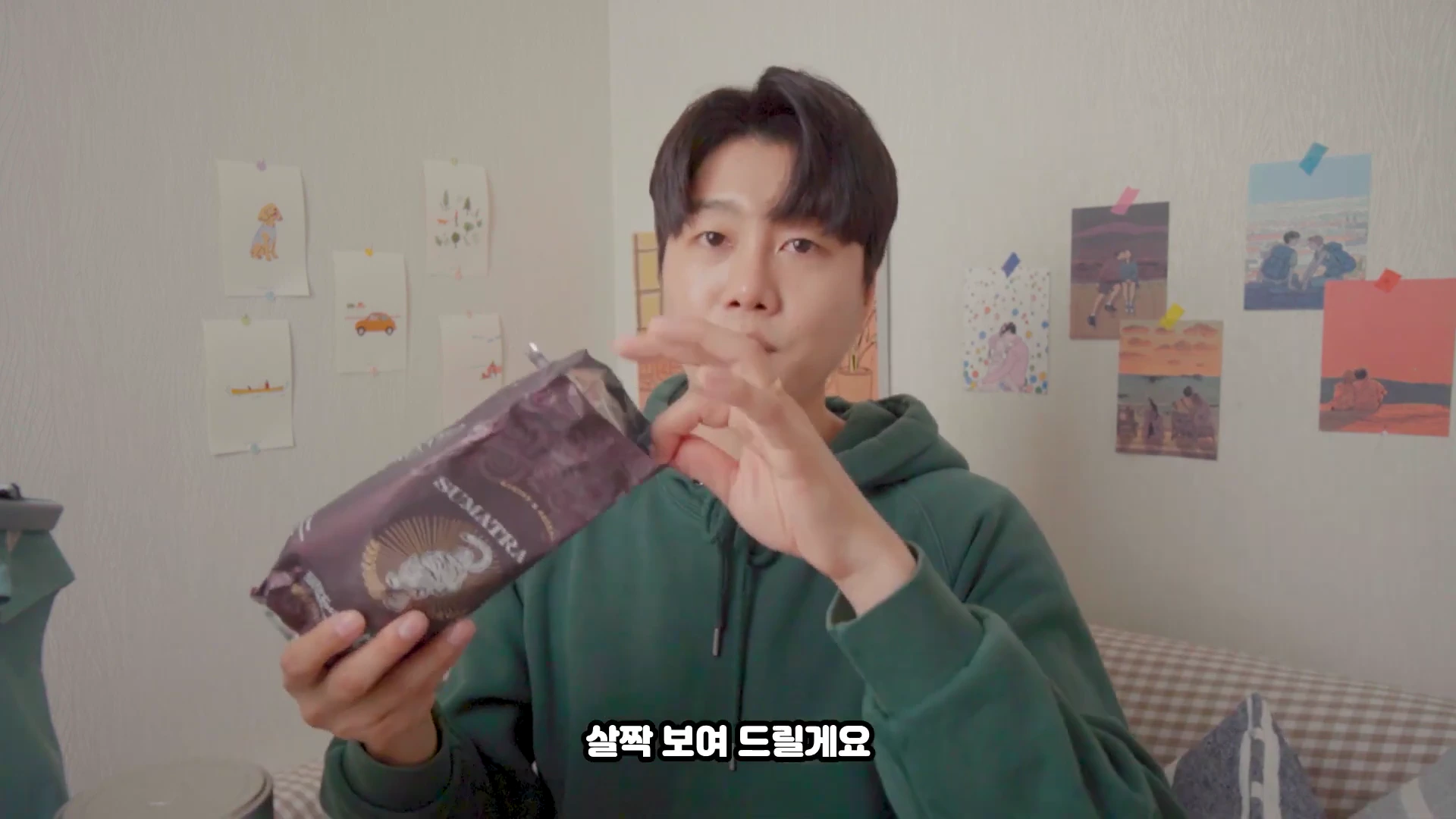 초록색 후드티를 입은 남성이 스타벅스 원두 봉투를 손에 들고 보여주고 있다.