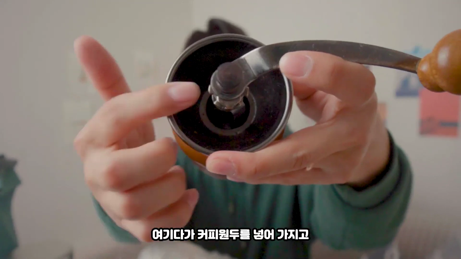 한 사람이 수동 커피 그라인더의 상단 투입구를 손가락으로 가리키고 있는 모습