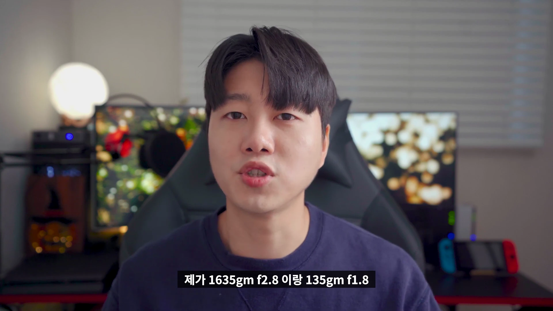 실내에서 카메라를 보며 이야기하는 남성, 하단에 렌즈 모델명이 적힌 자막이 떠 있다.