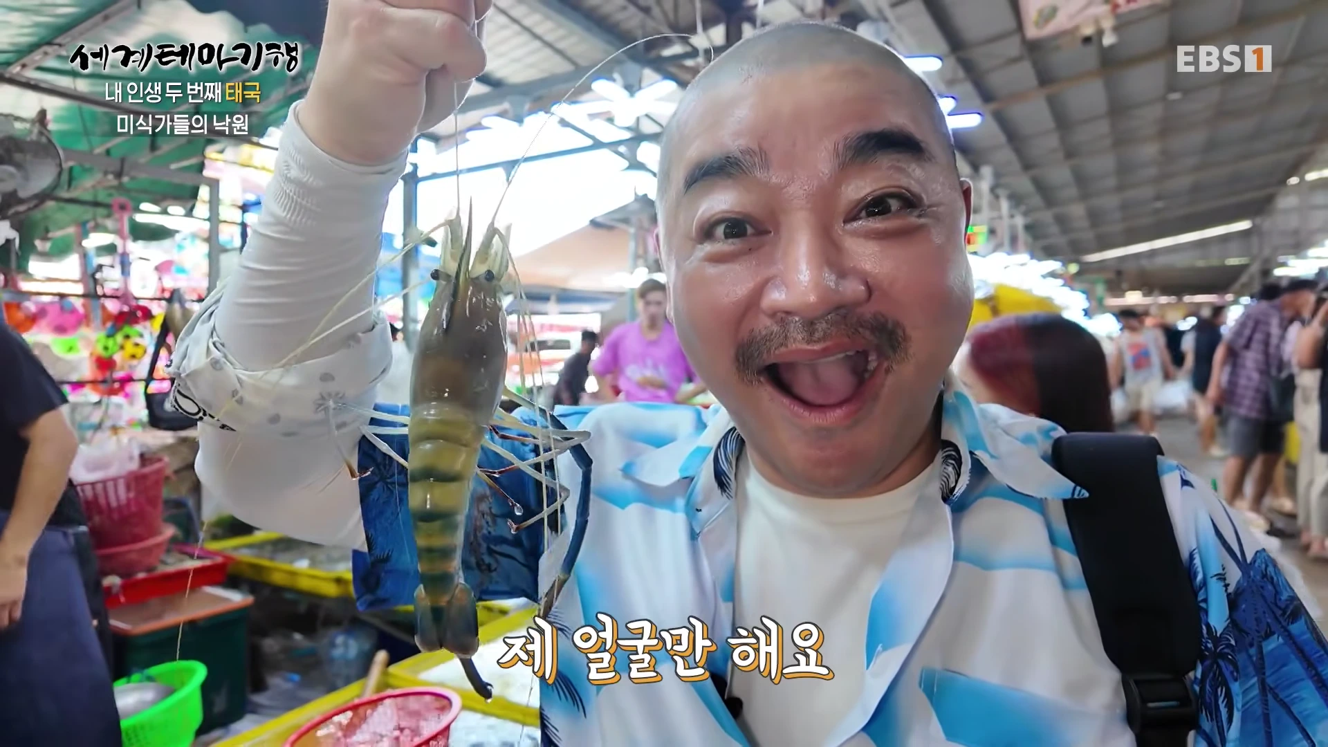 태국 시장에서 한 남성이 자신의 얼굴 크기만 한 커다란 민물새우를 들어 보이며 놀란 표정을 짓고 있다.