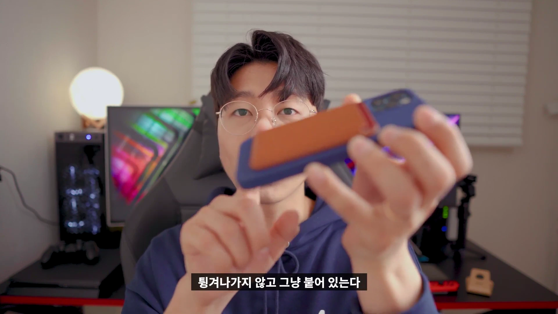 안경을 쓴 남성이 맥세이프 카드지갑이 부착된 아이폰을 손에 들고 보여주고 있다.