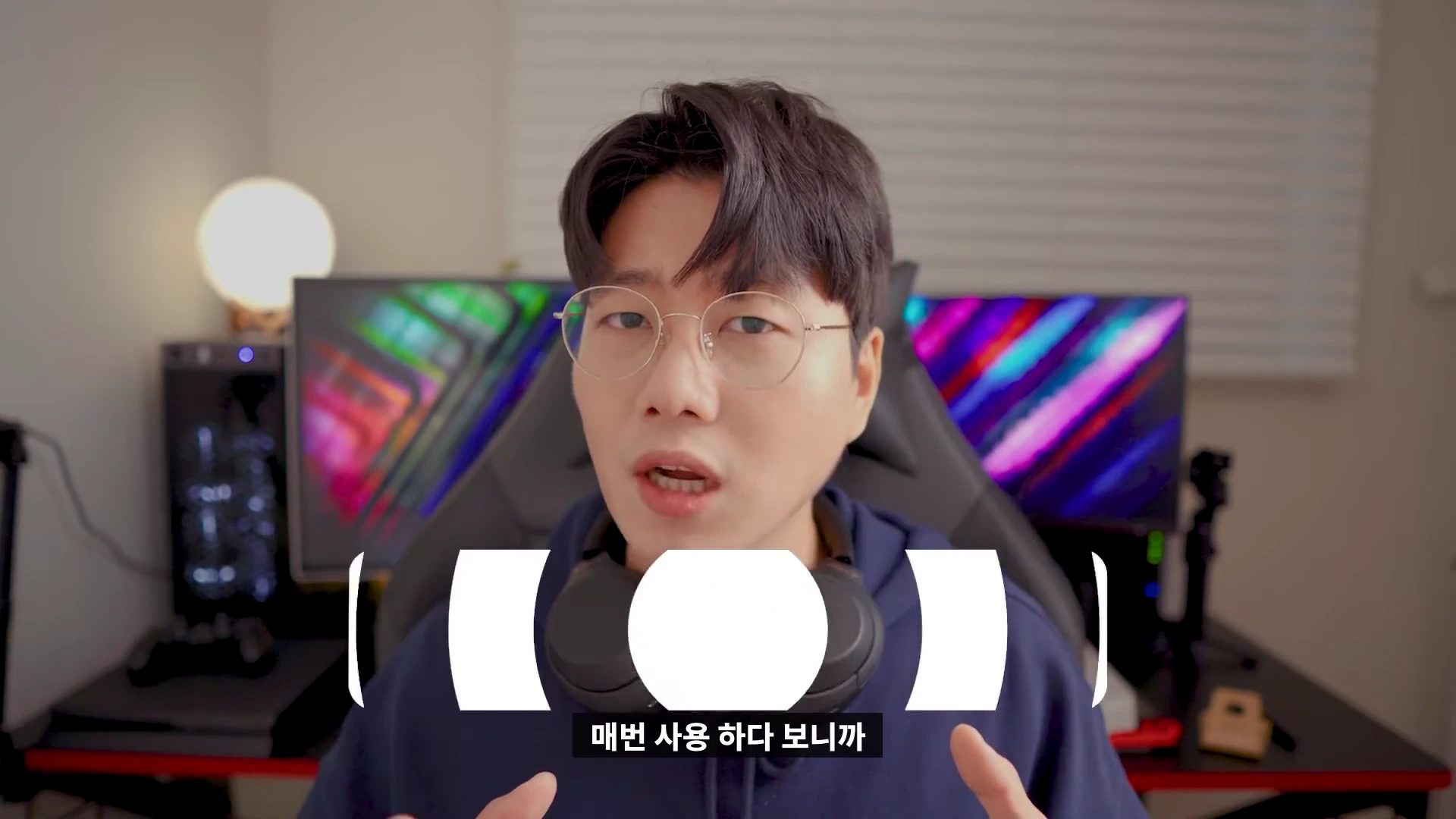 안경을 쓴 남성이 헤드폰을 목에 걸고 카메라를 보며 이야기하는 모습