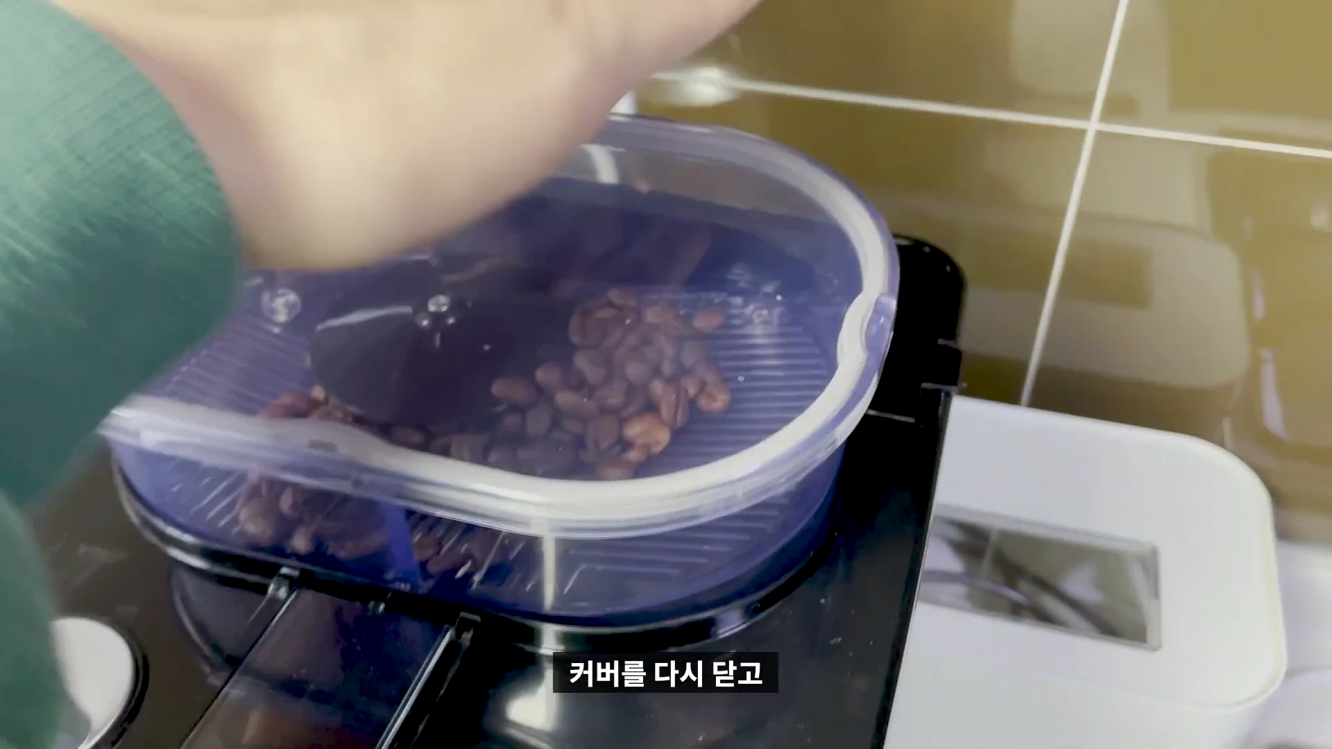 커피머신 상단 원두 용기에 원두를 넣고 투명한 커버를 닫는 모습