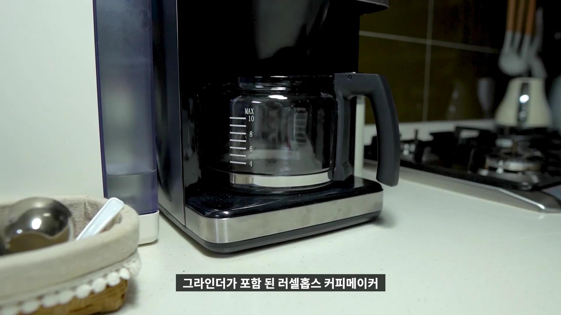 주방 조리대 위에 놓인 검은색 그라인더 내장형 커피메이커와 유리 서버