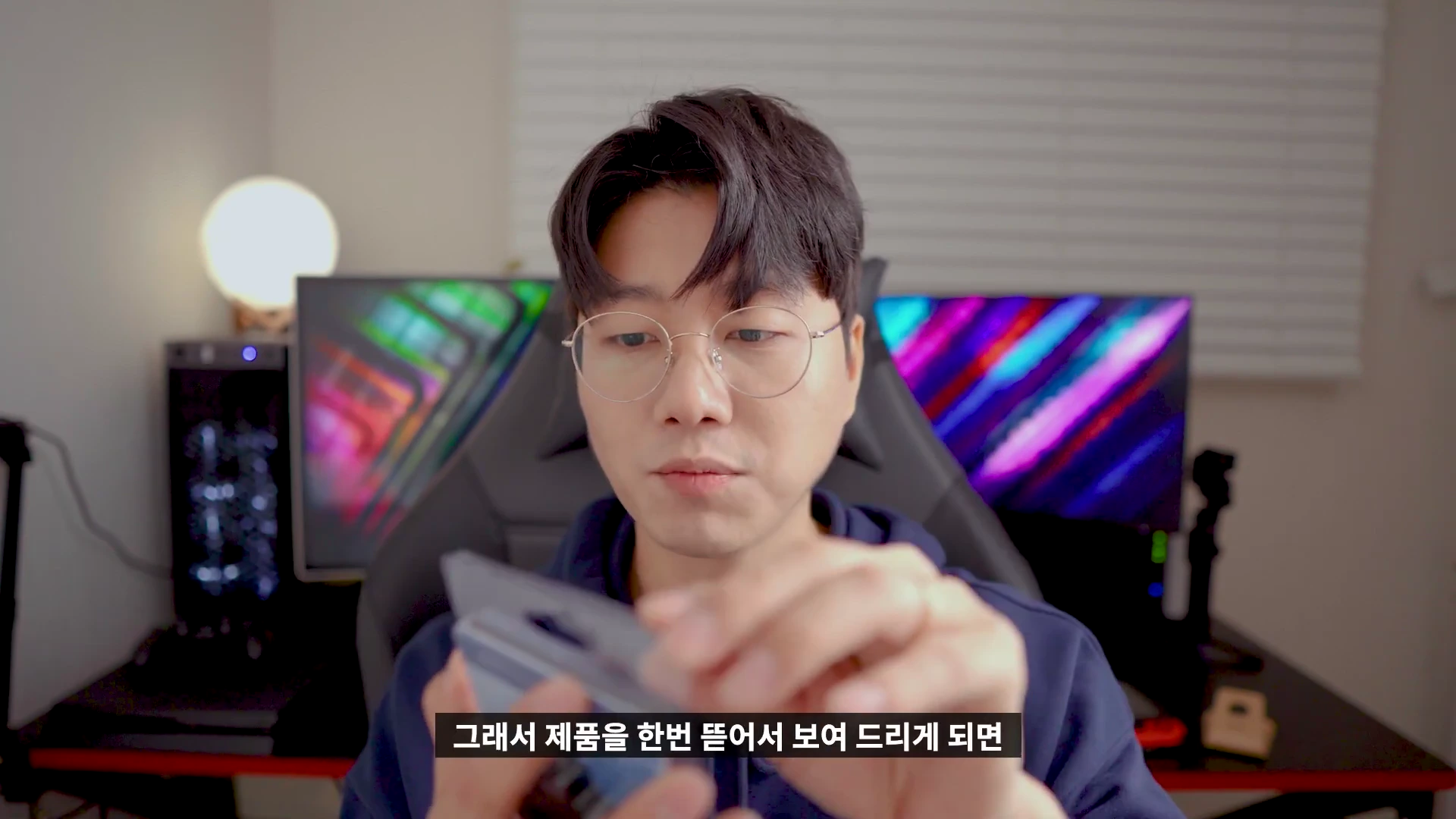 안경을 쓴 남성이 책상에 앉아 손에 든 작은 USB 테스터기 제품 패키지를 살펴보고 있다.