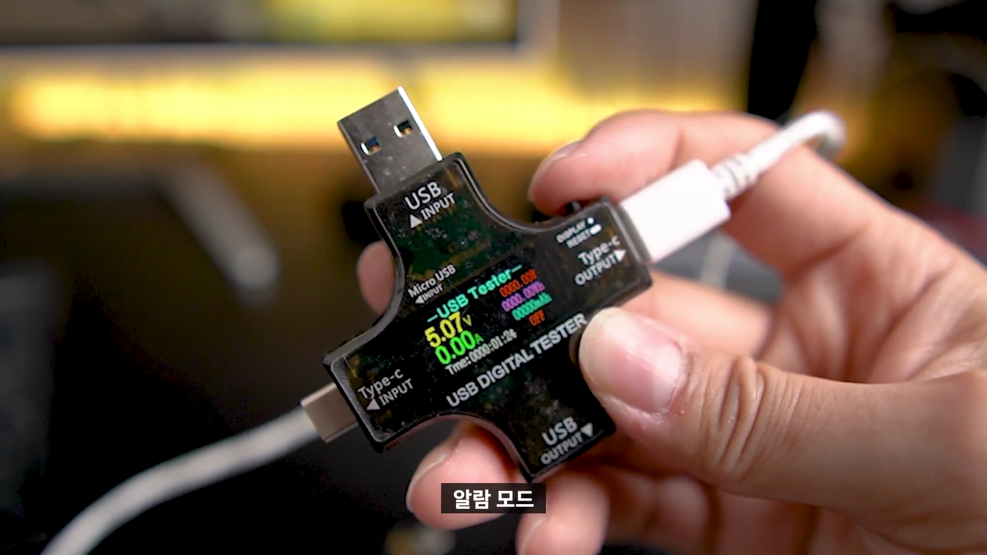 손에 들린 USB 전압 측정기 화면에 전압과 전류 수치가 표시되고 있다.