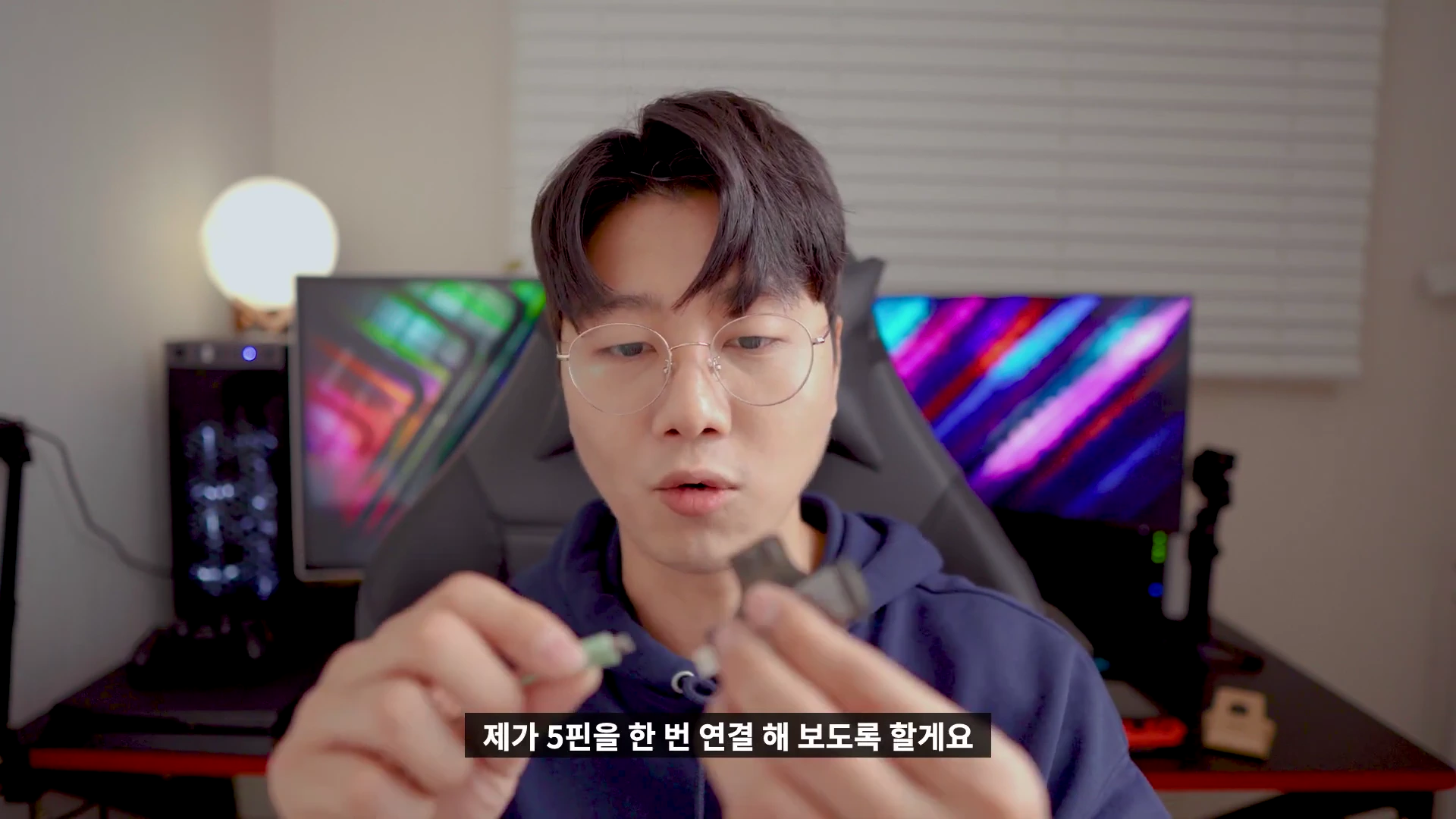 안경을 쓴 남성이 책상에 앉아 마이크로 5핀 케이블과 변환 젠더를 손에 들고 설명하는 모습