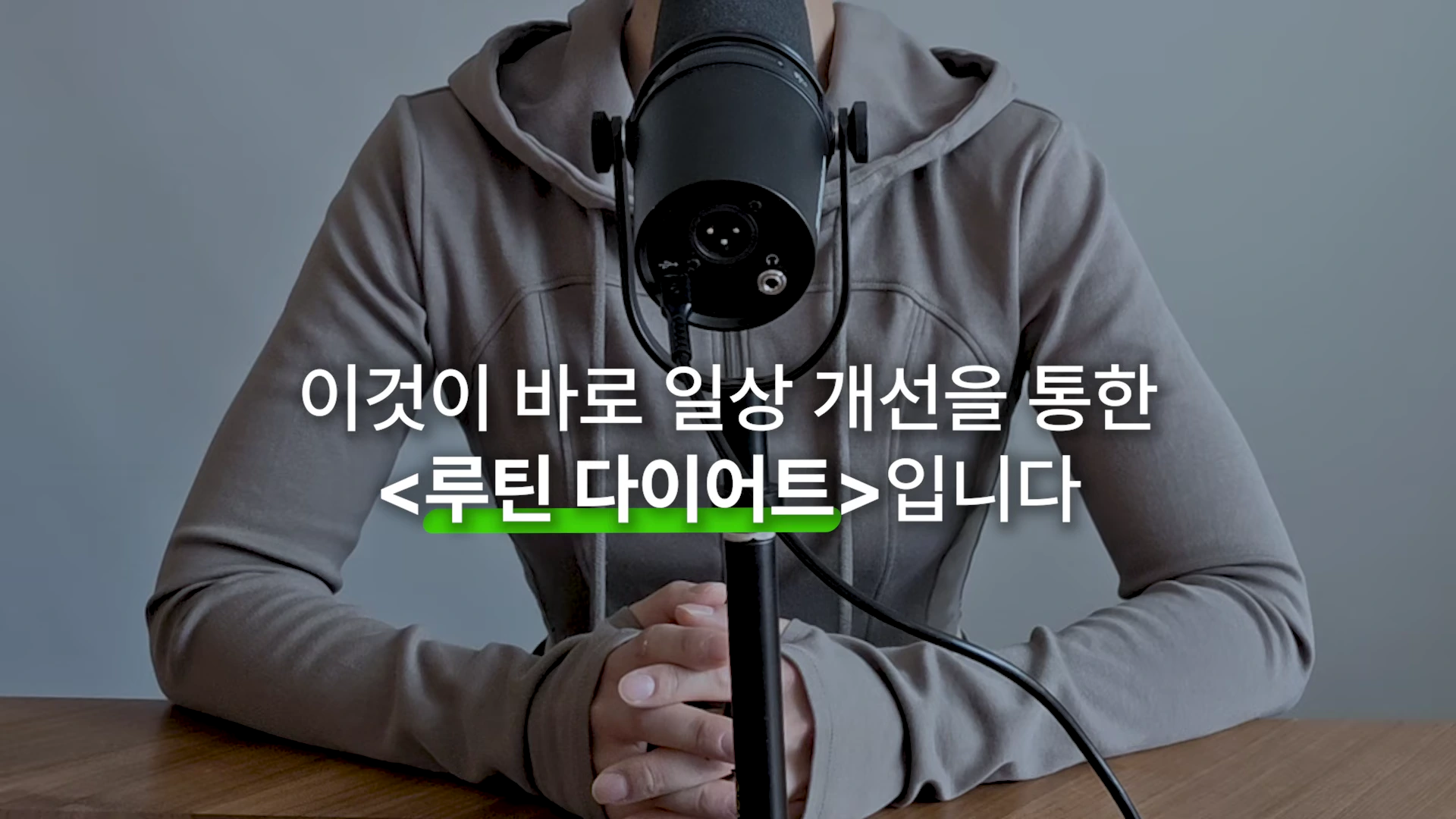 회색 후드티를 입은 사람이 마이크 앞에 앉아 있는 모습