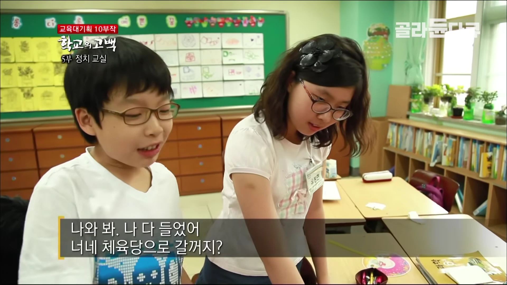 교실에서 안경을 쓴 남학생과 여학생이 서로 대화를 나누고 있는 모습