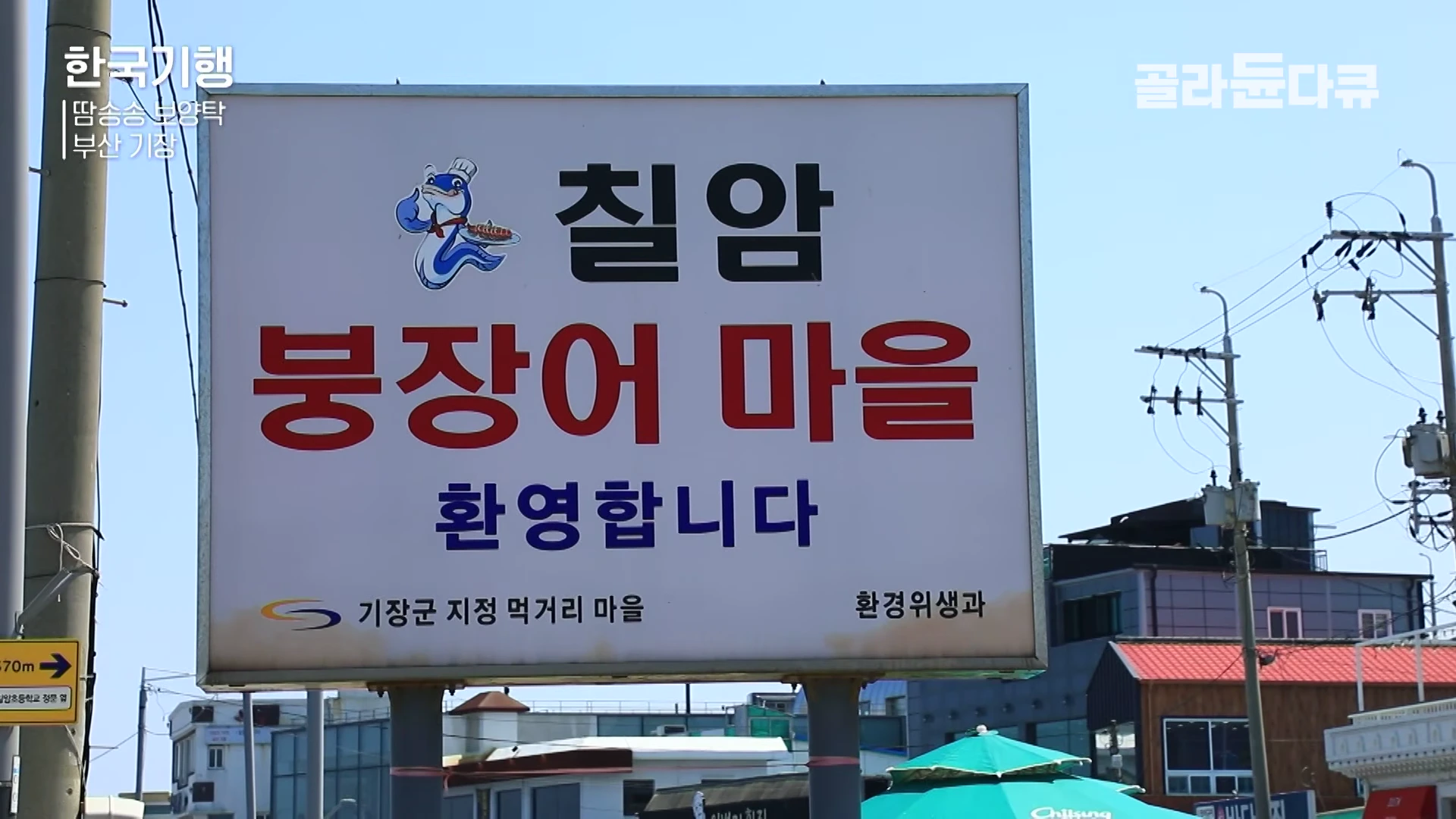 '칠암 붕장어 마을 환영합니다'라고 적힌 대형 야외 간판과 파란 하늘.