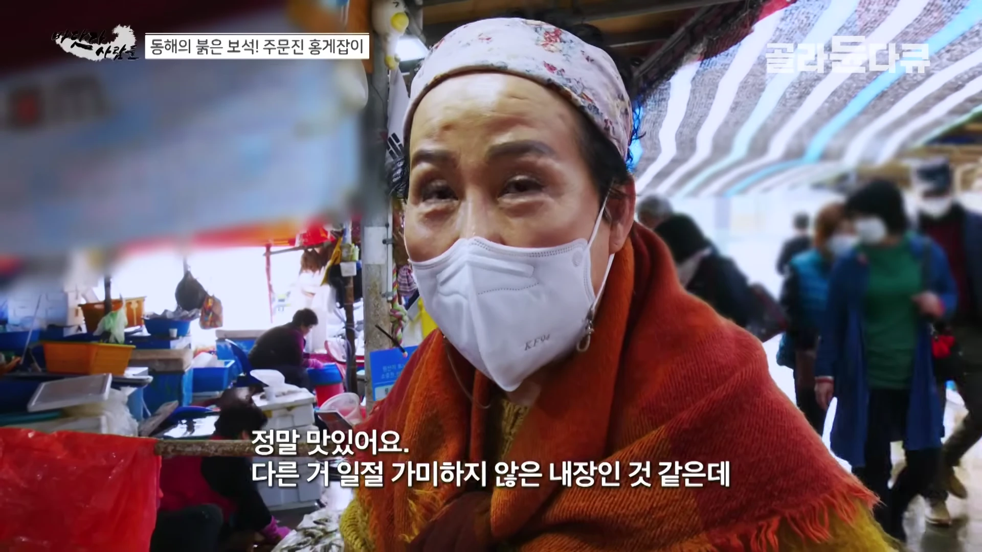 두건을 쓰고 마스크를 착용한 중년 여성이 시장에서 인터뷰하는 모습