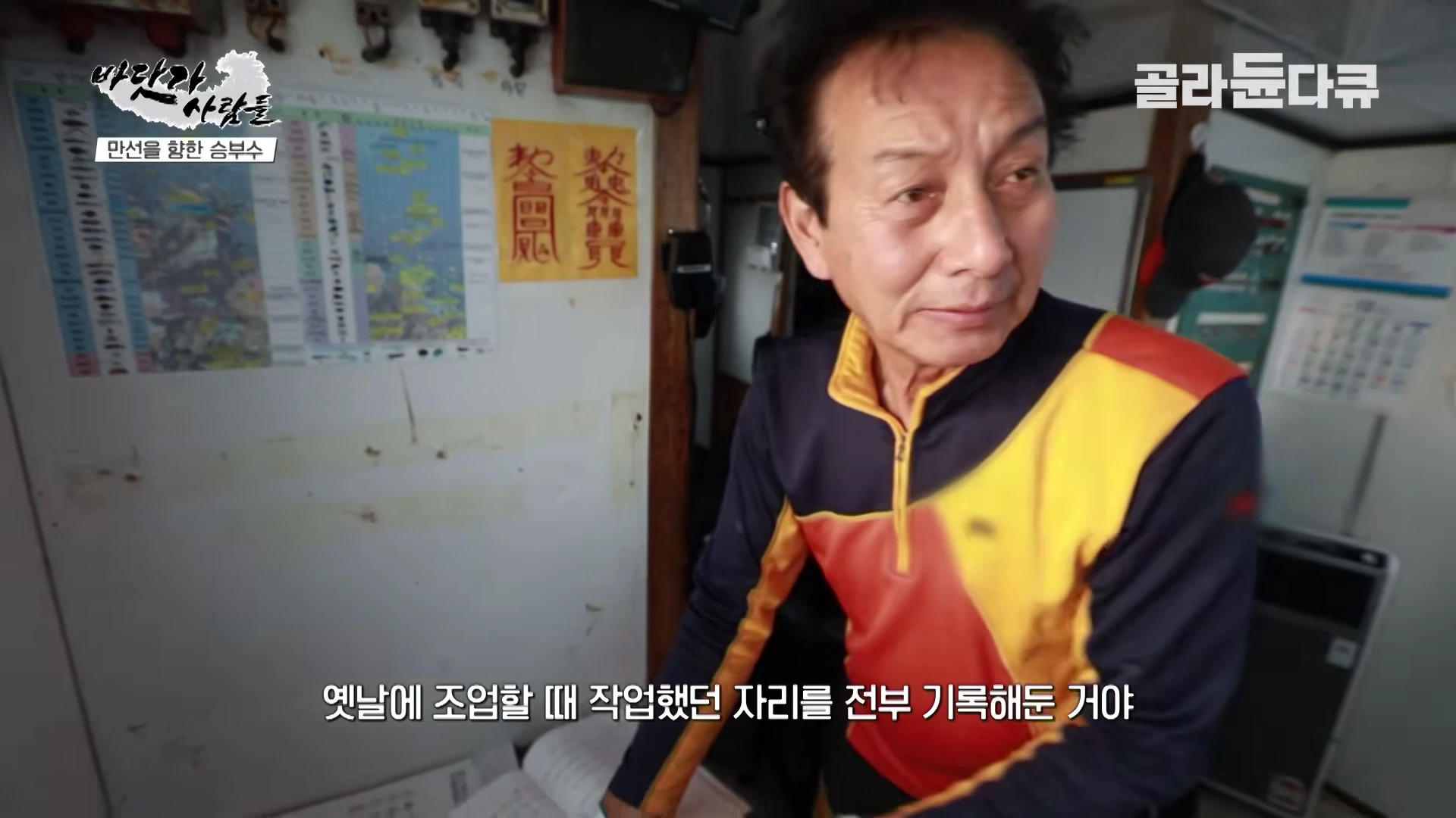 선실 안에서 작업 일지를 가리키며 설명하는 중년 남성 선장