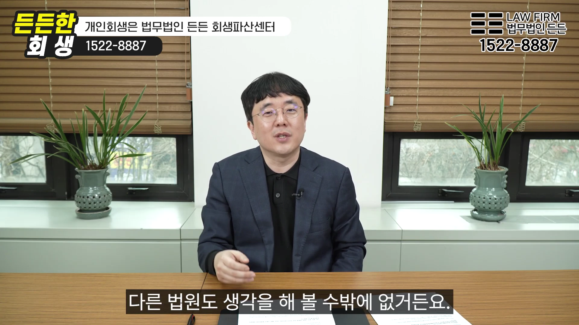안경을 쓴 남성 변호사가 사무실 책상에 앉아 카메라를 보며 설명하고 있는 모습