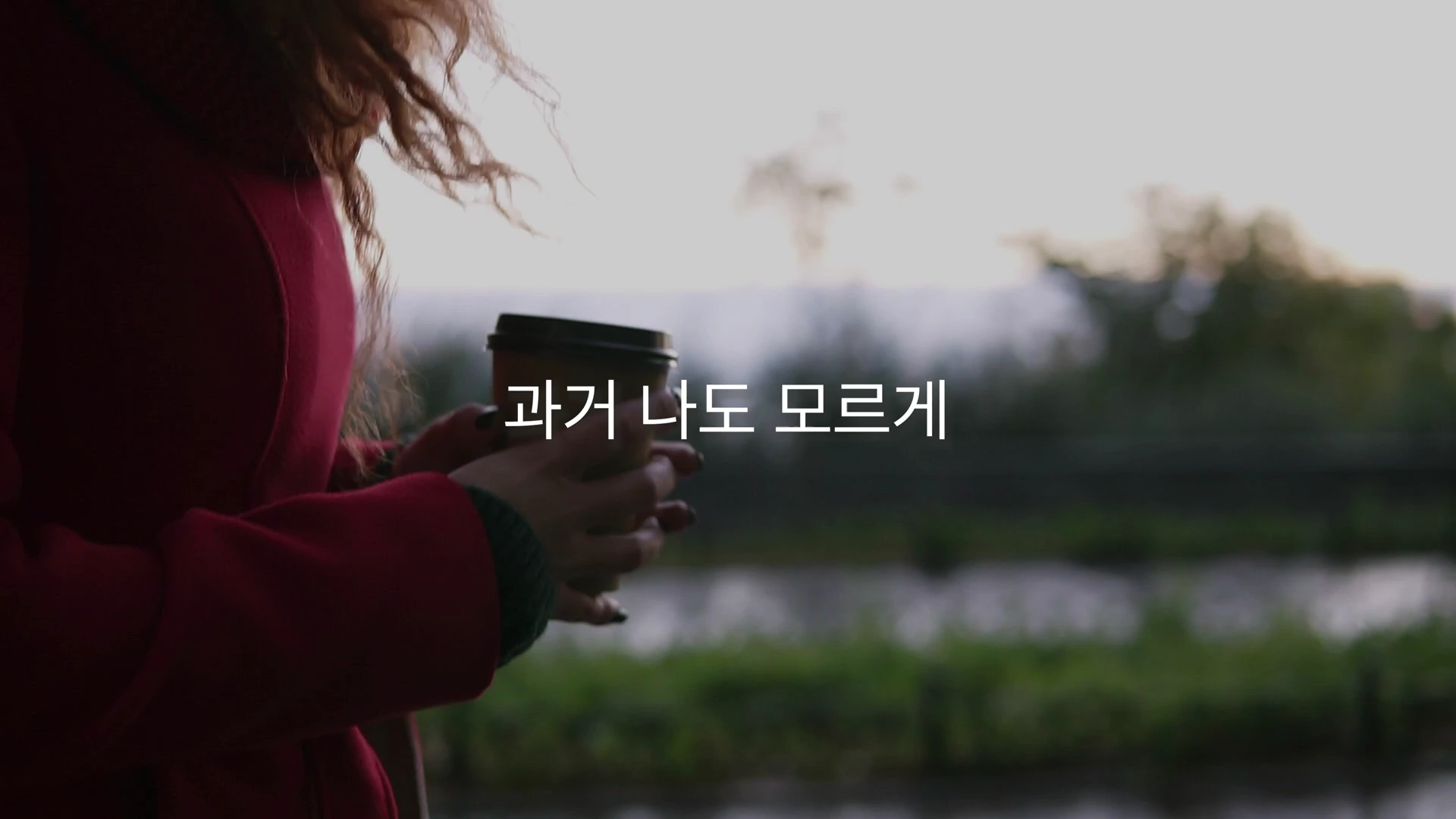 붉은 코트를 입은 사람이 커피 컵을 들고 서 있는 모습과 '과거 나도 모르게'라는 자막