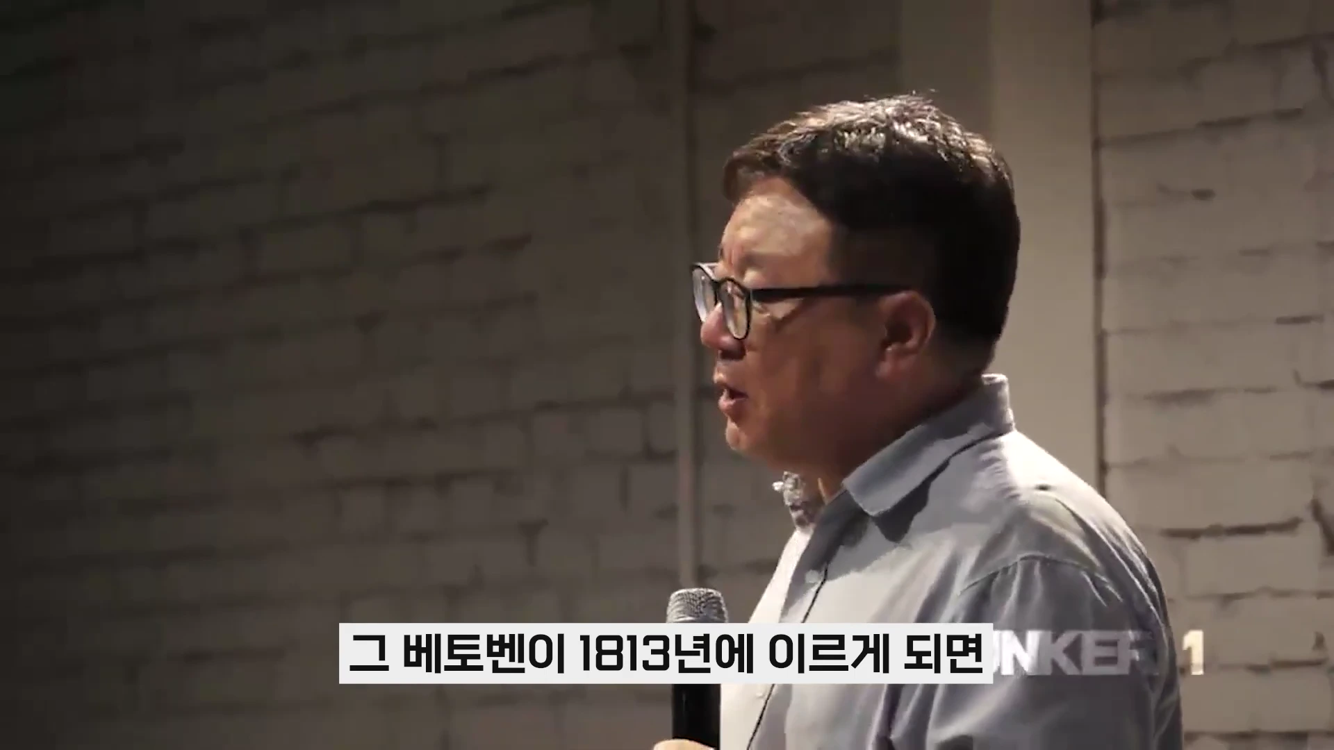 안경을 쓴 중년 남성이 마이크를 잡고 강연하는 모습