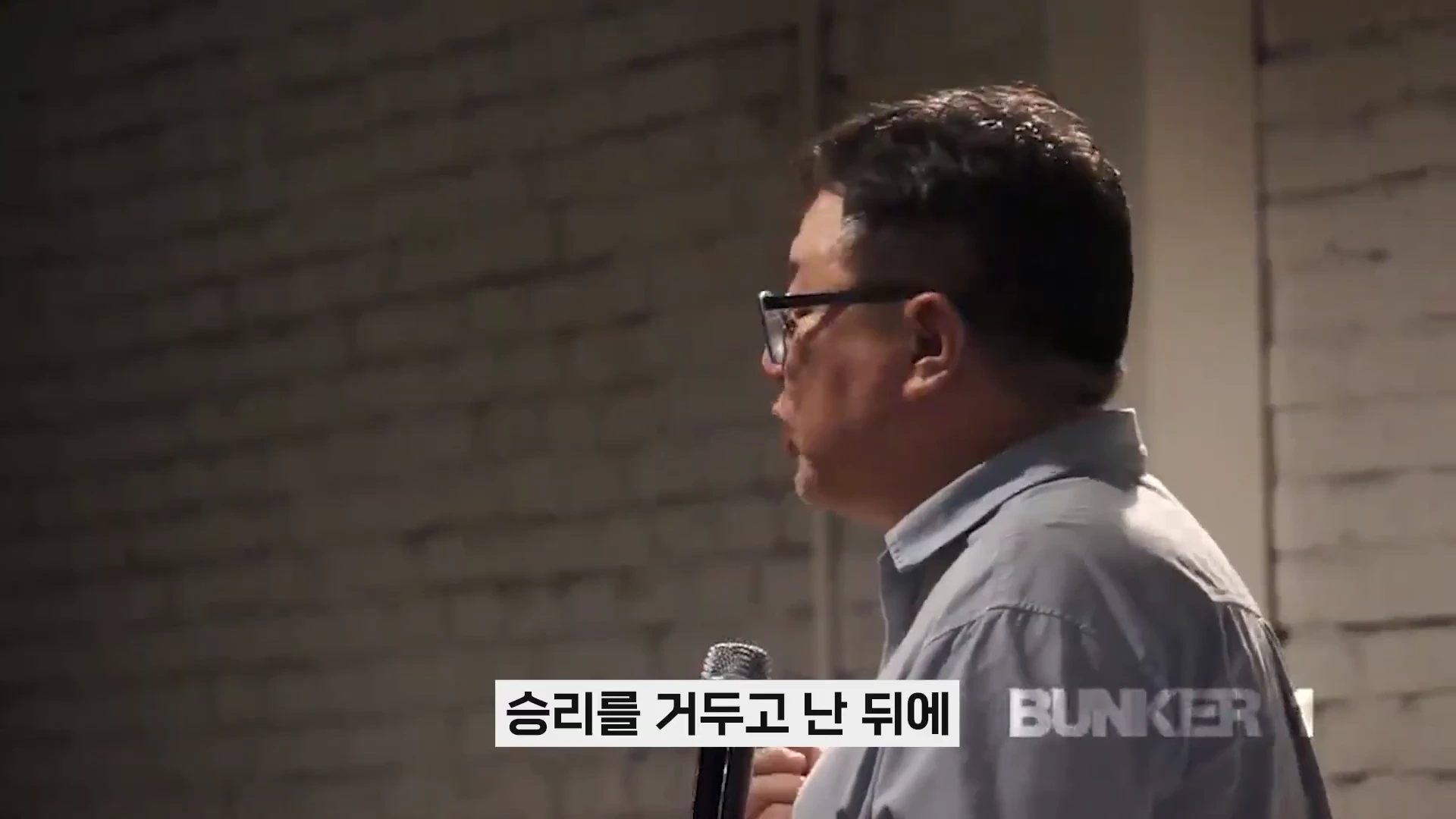 안경을 쓴 남성이 마이크를 들고 강연하는 옆모습