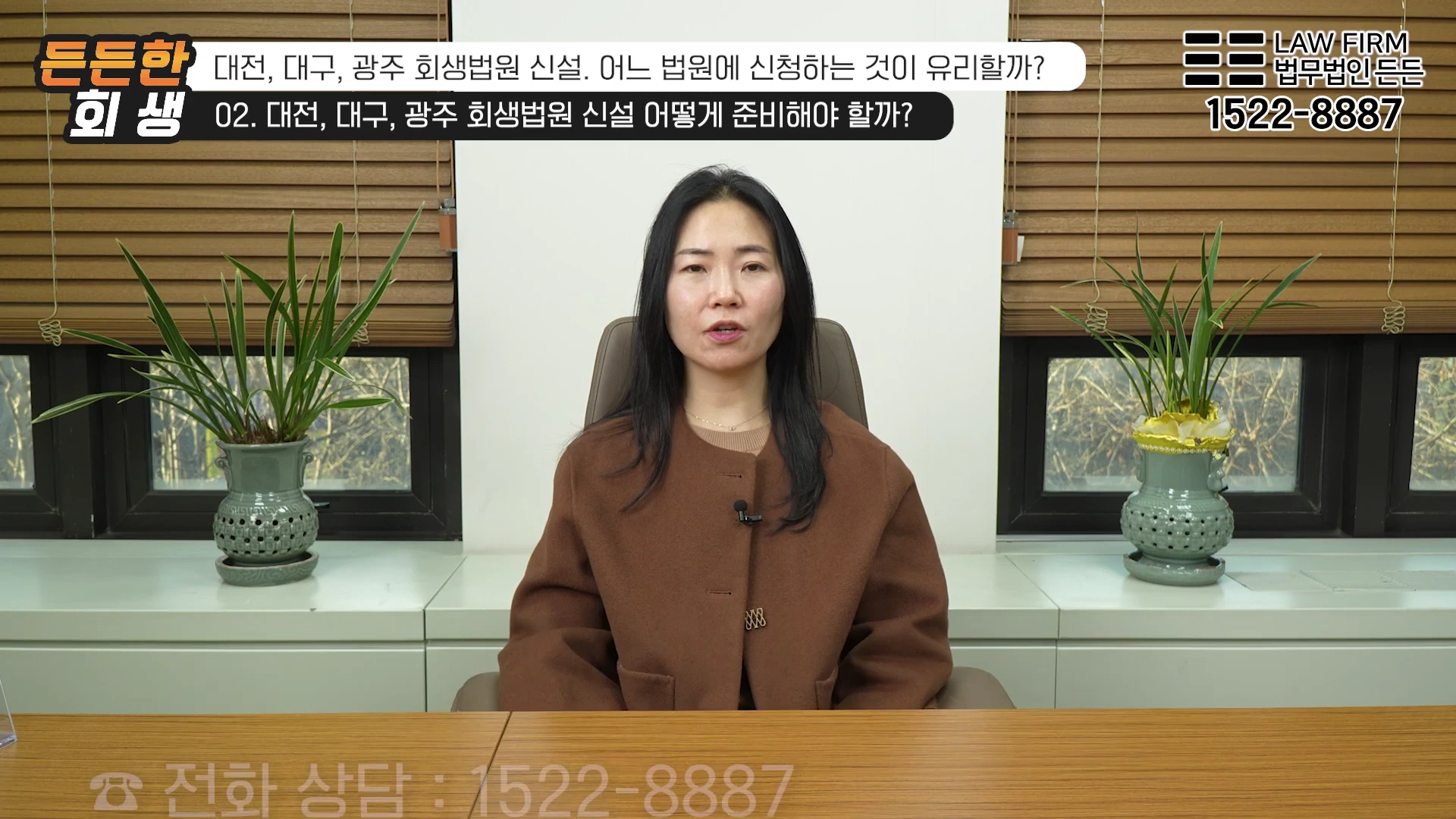 갈색 재킷을 입은 여성이 사무실 책상 앞에 앉아 정면을 바라보며 이야기하고 있다.