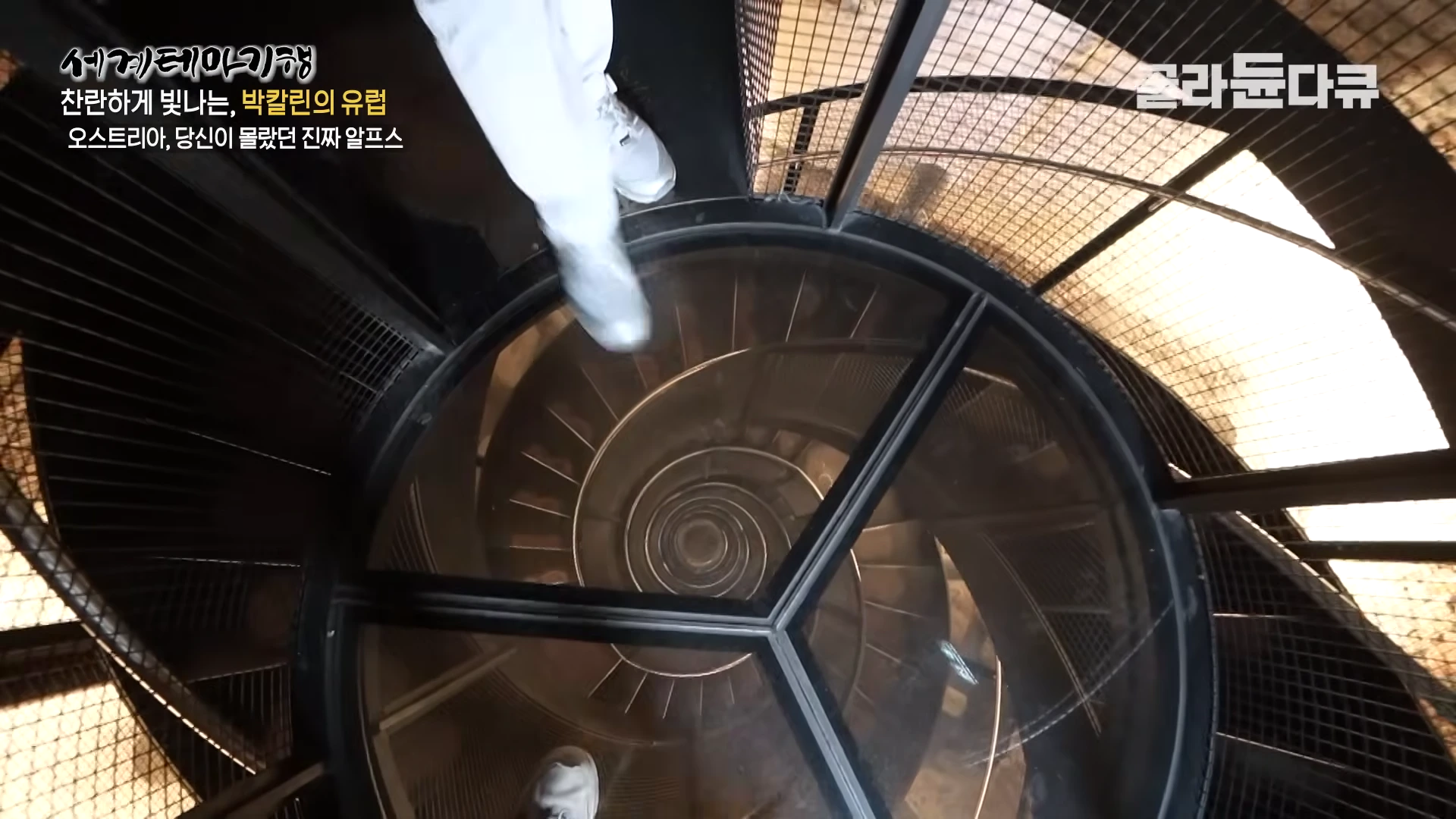 투명한 바닥 아래로 좁고 가파르게 이어지는 나선형 계단이 내려다보이는 모습