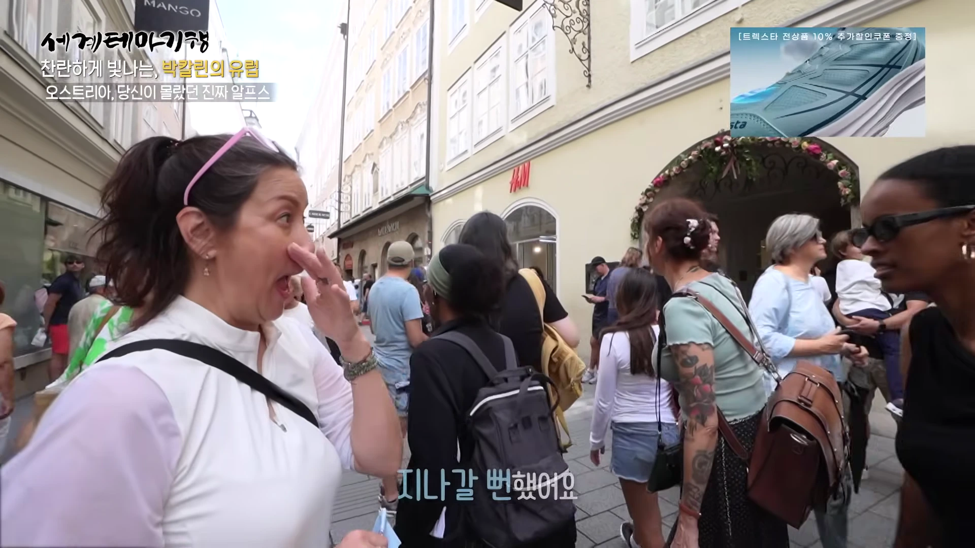 잘츠부르크의 번화한 거리에서 놀란 표정으로 손을 입에 대고 있는 여성과 주변을 지나는 여행객들