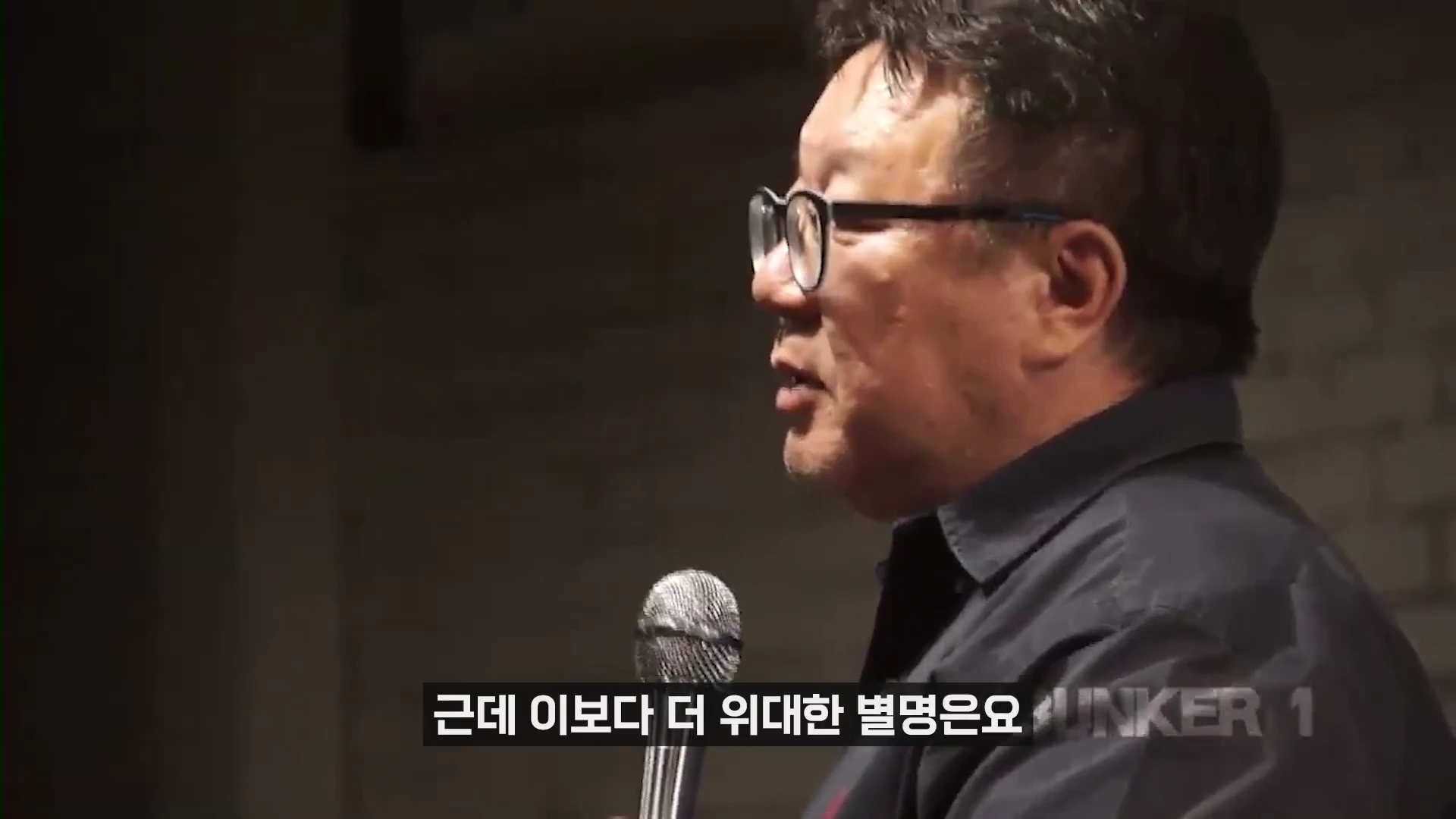 안경을 쓴 중년 남성이 마이크를 잡고 강연하는 옆모습
