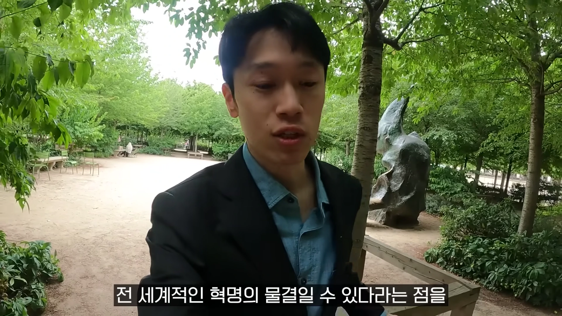 공원 산책로에서 검은 재킷을 입은 남성이 카메라를 보며 이야기하고 있고 하단에는 자막이 떠 있다.