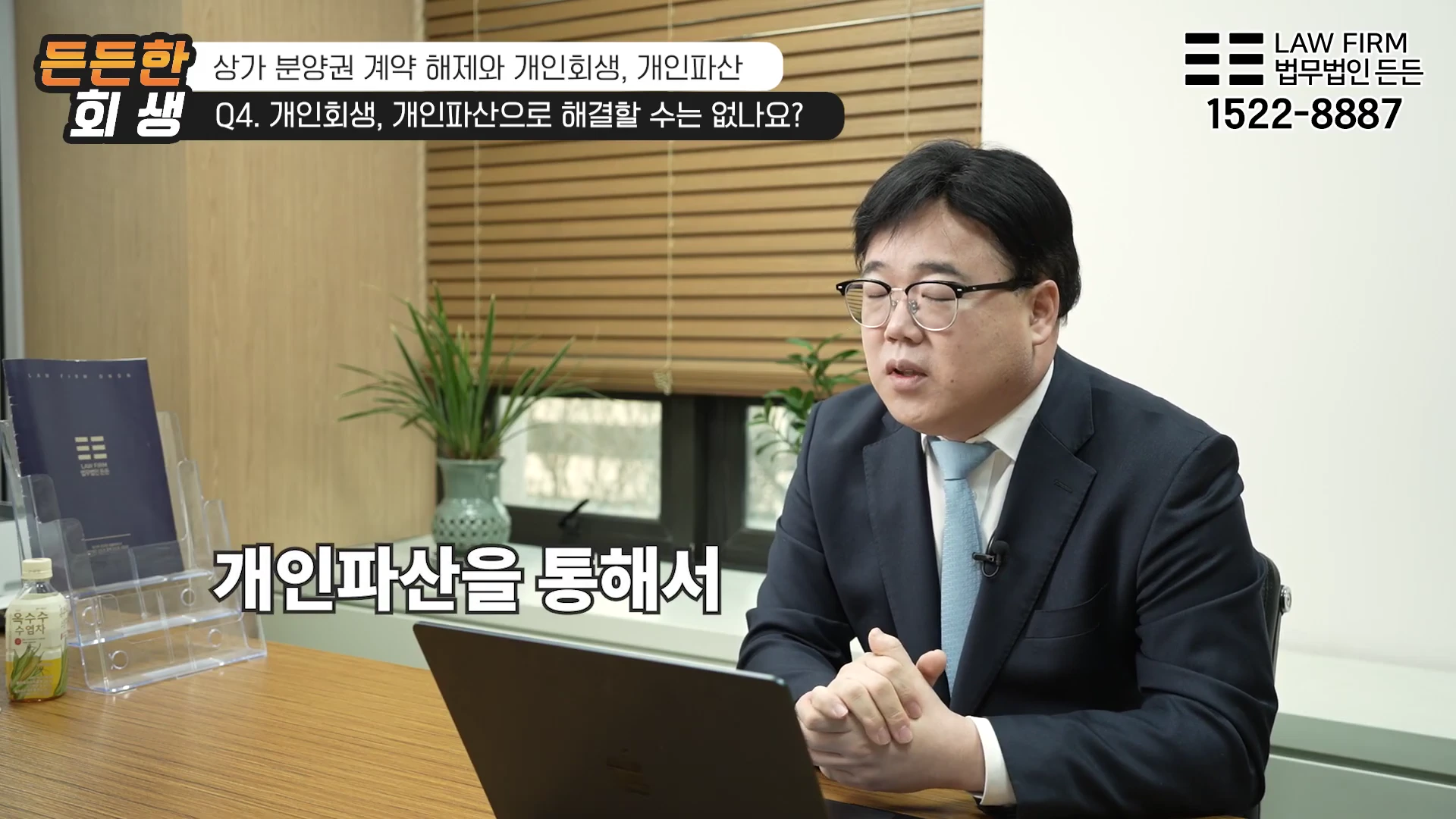안경을 쓴 남성 변호사가 사무실 책상에 앉아 인터뷰를 진행하고 있으며, 화면 상단에는 관련 주제와 연락처가 자막으로 표시되어 있습니다.